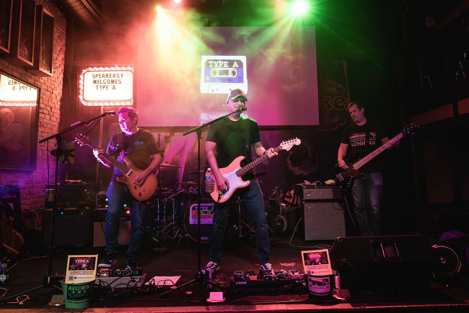 Musicians playing guitars on stage with green and red lighting effects during a live performance.