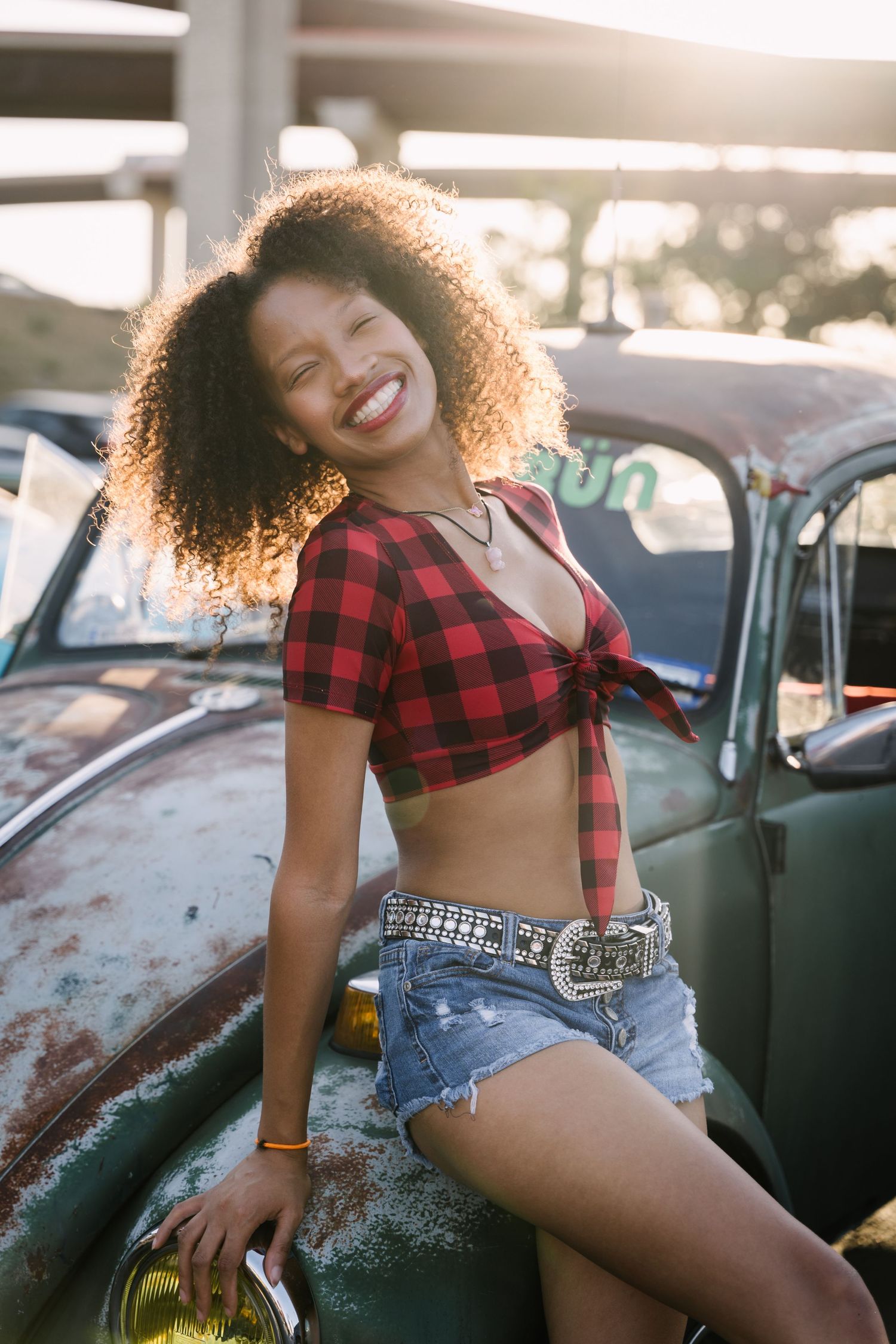Vintage car photoshoot featuring red plaid shirt and denim shorts styling.