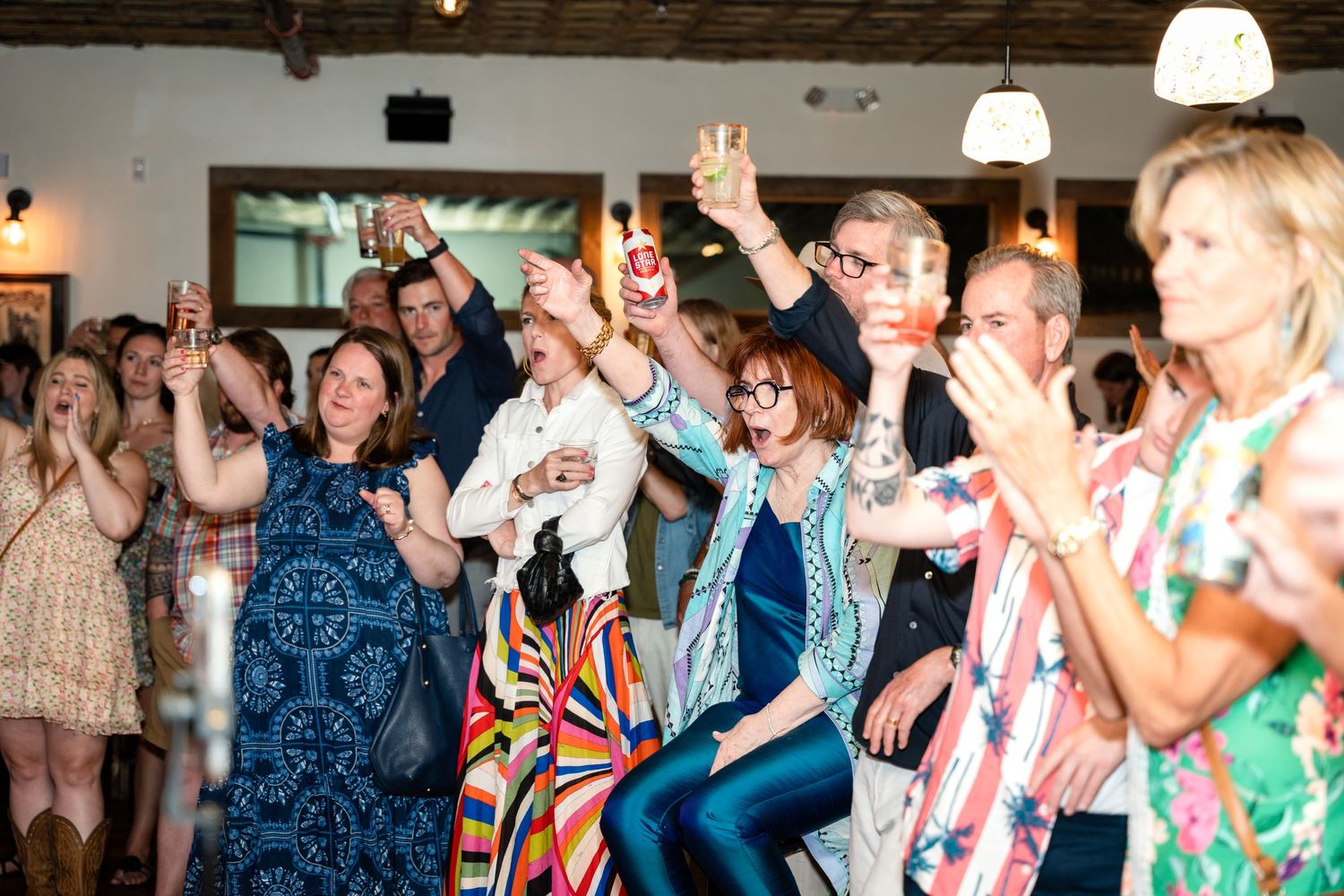 Enthusiastic crowd raising their hands and cheering during an indoor celebration.