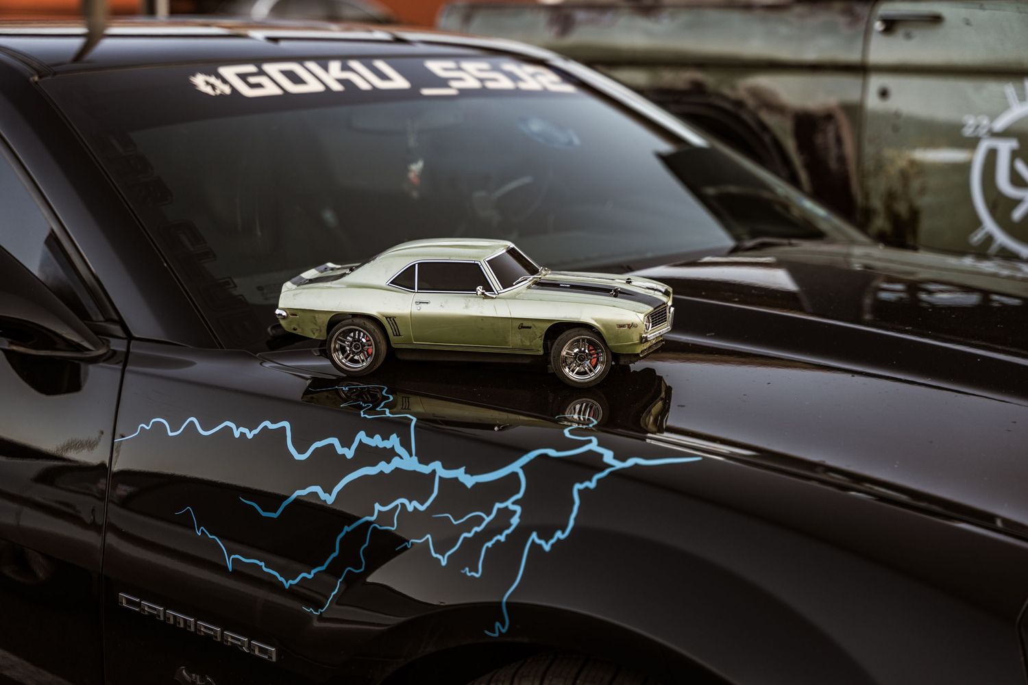 Small vintage car model displayed on black car hood with lightning graphic decal.