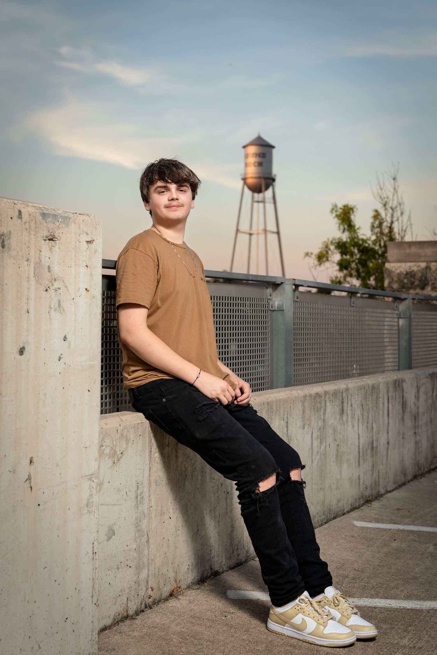 Someone poses against concrete wall with vintage water tower visible in background.