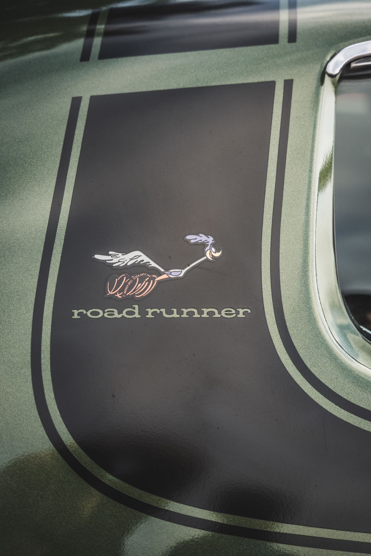 Close-up detail of vintage Road Runner decal and stripe on green car panel.