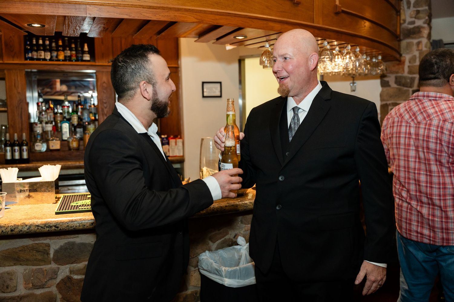 Two people share drinks and conversation at a rustic wooden bar during an event.