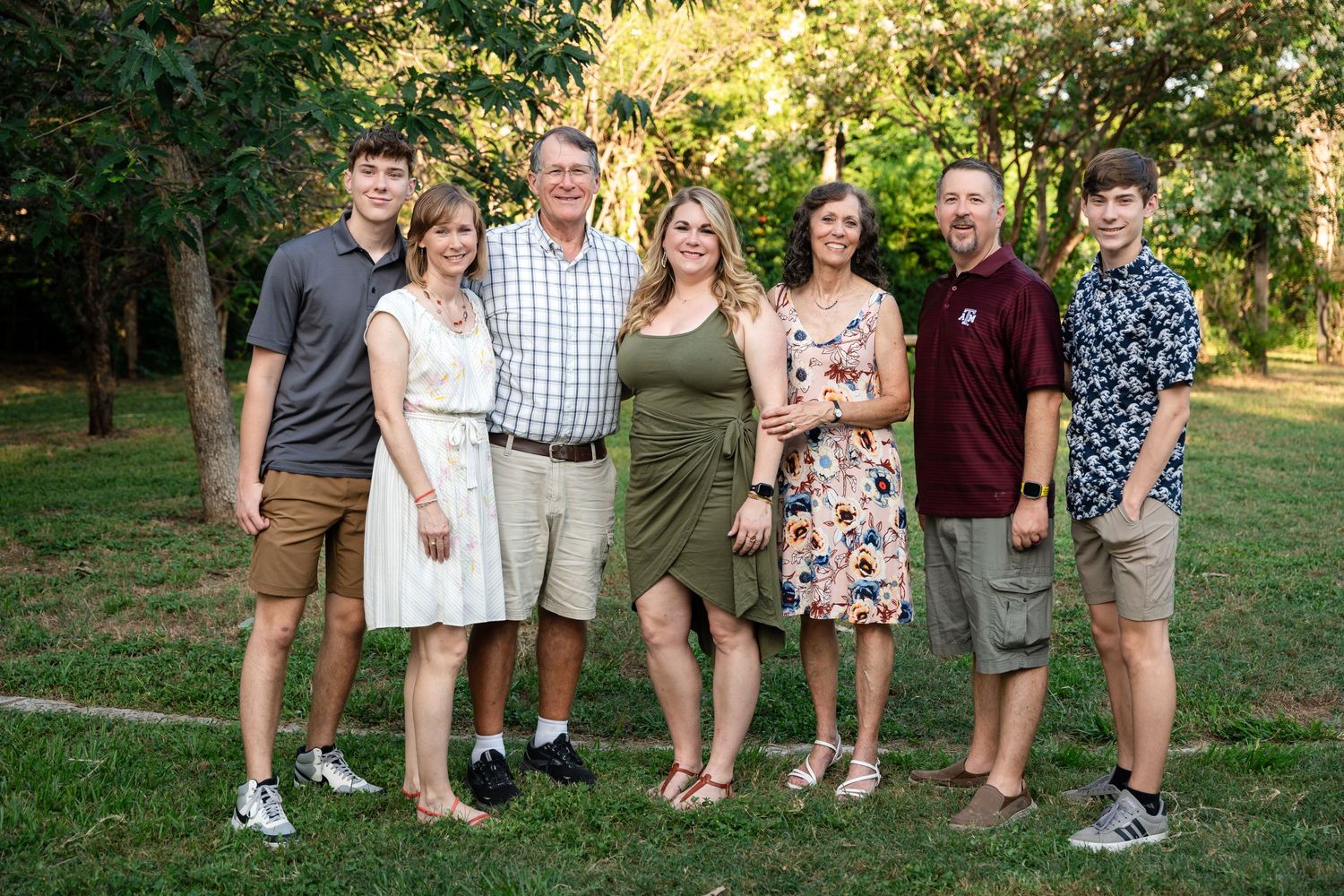 A casual family group poses together outdoors during a summer gathering.