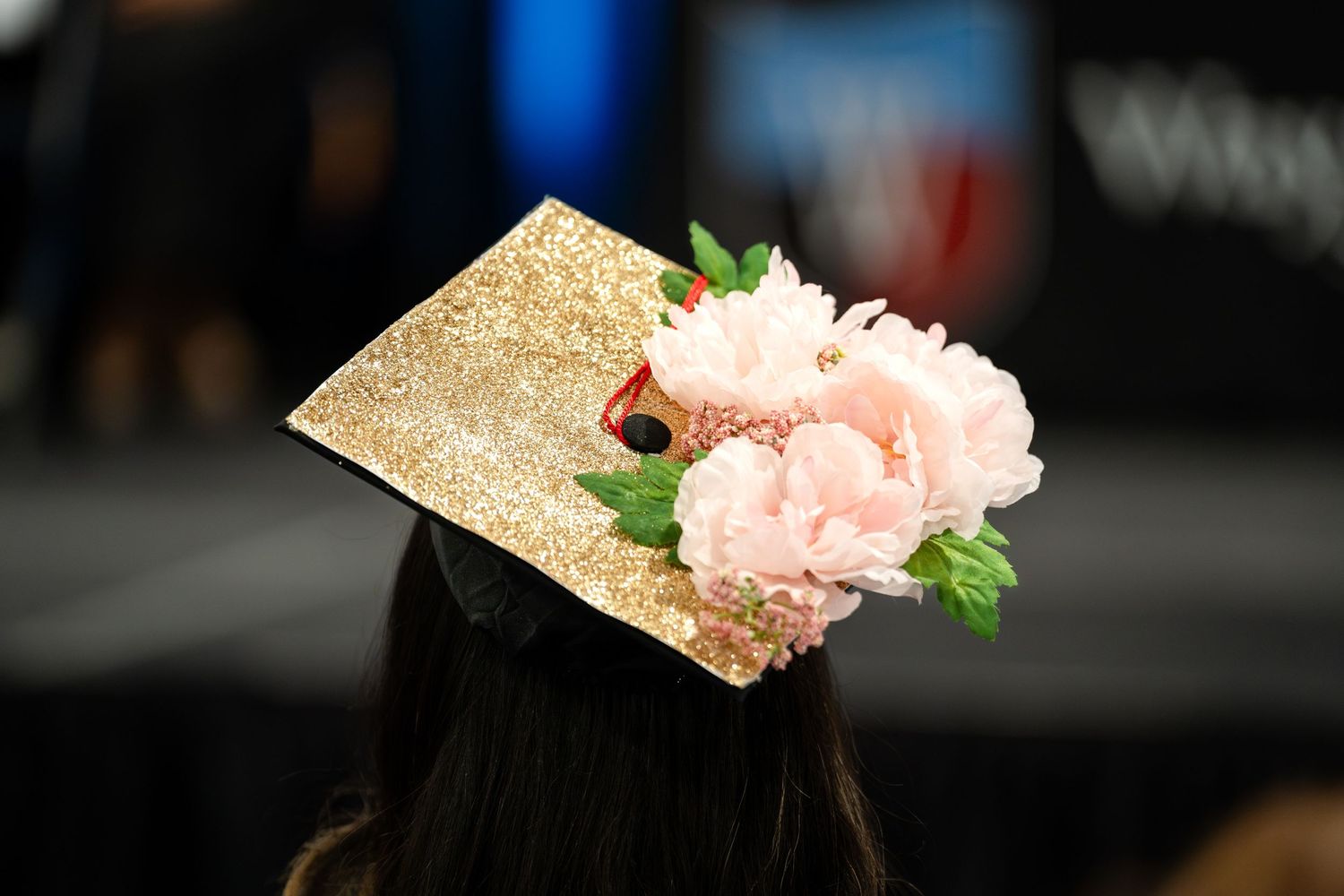 Graduation cap adorned with gold glitter and pink flower decoration.