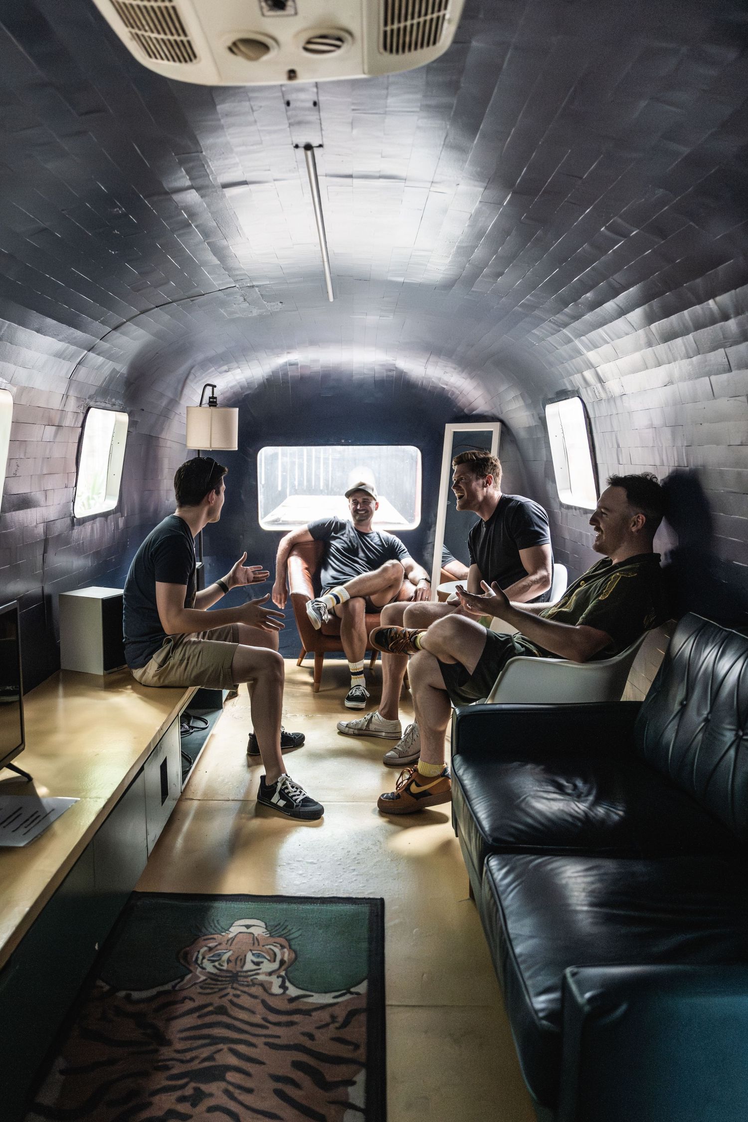 Musicians relaxing in vintage Airstream trailer with leather seating and dim lighting.