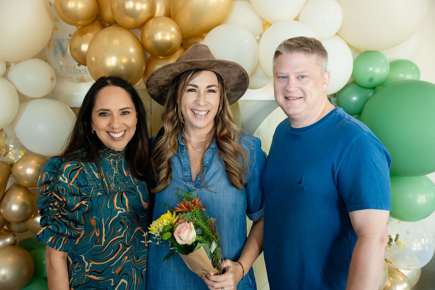 Group photo in front of decorative balloon arch with white, gold and green balloons.