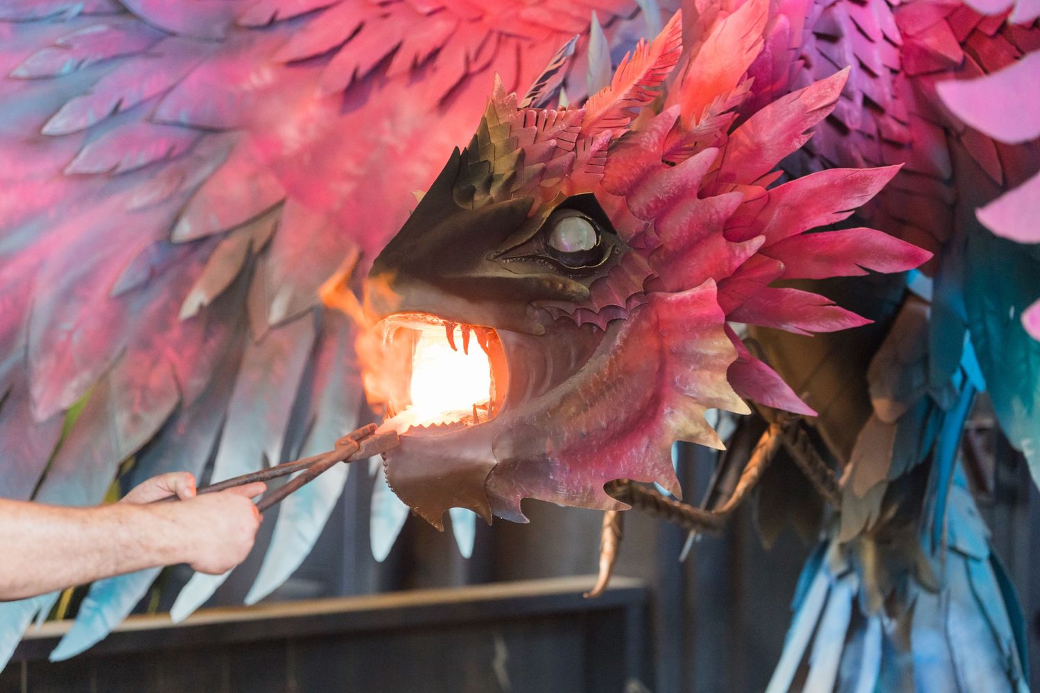Close-up of a colorful dragon prop with glowing eyes and pink feathered wings.