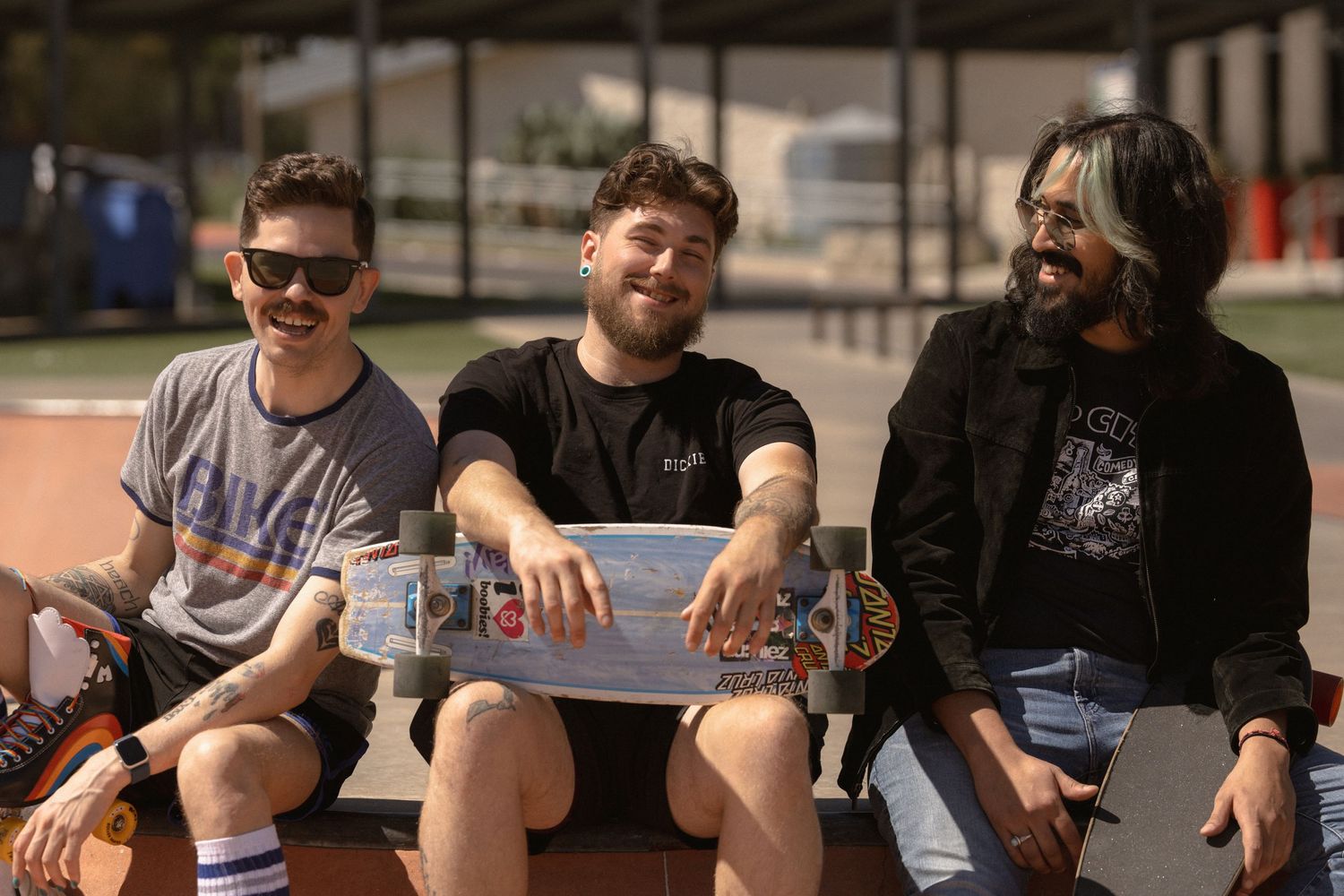 Three friends sitting together and laughing at skate park.