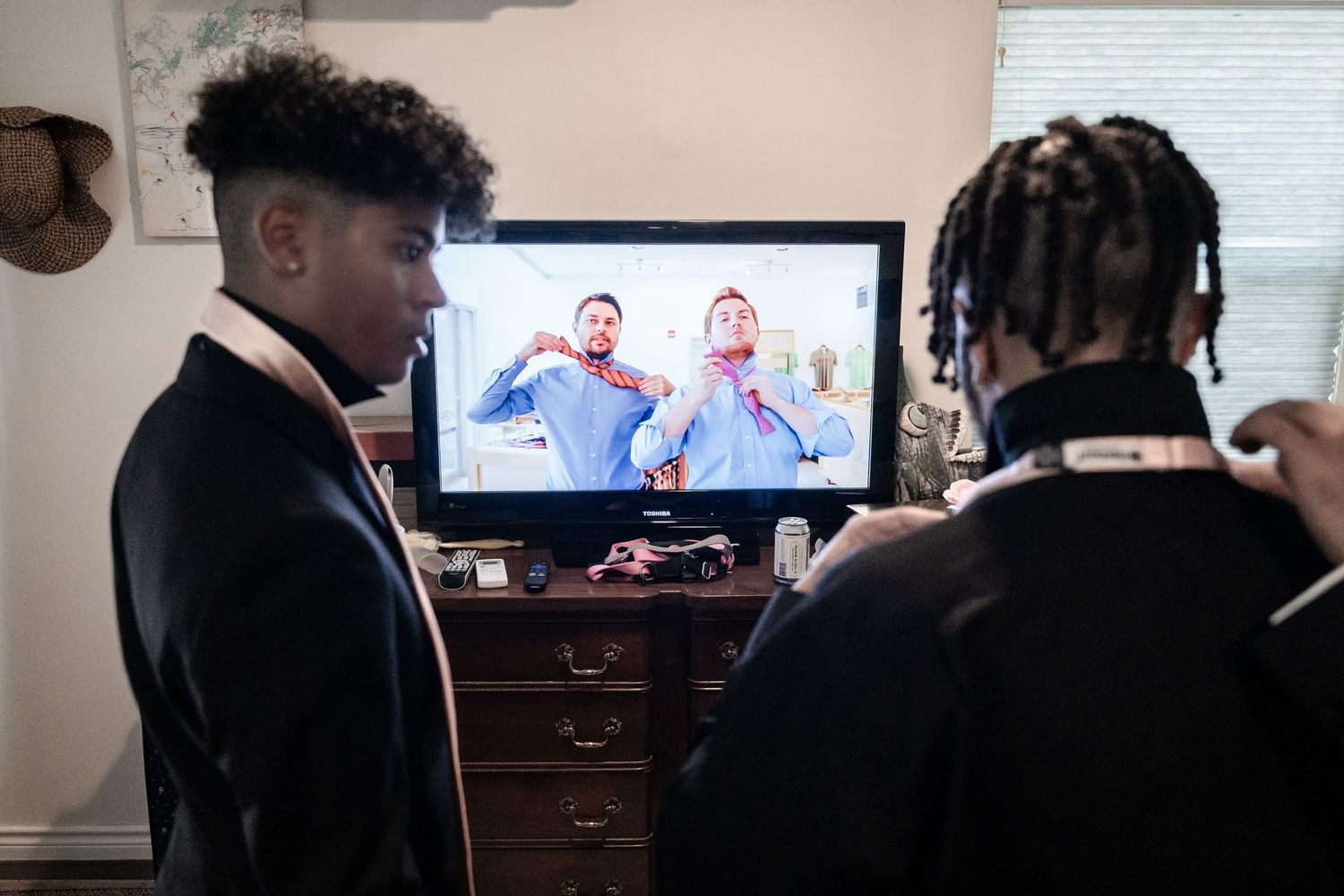 Wedding preparation scene with groomsmen watching a video screen while wearing formal suits.