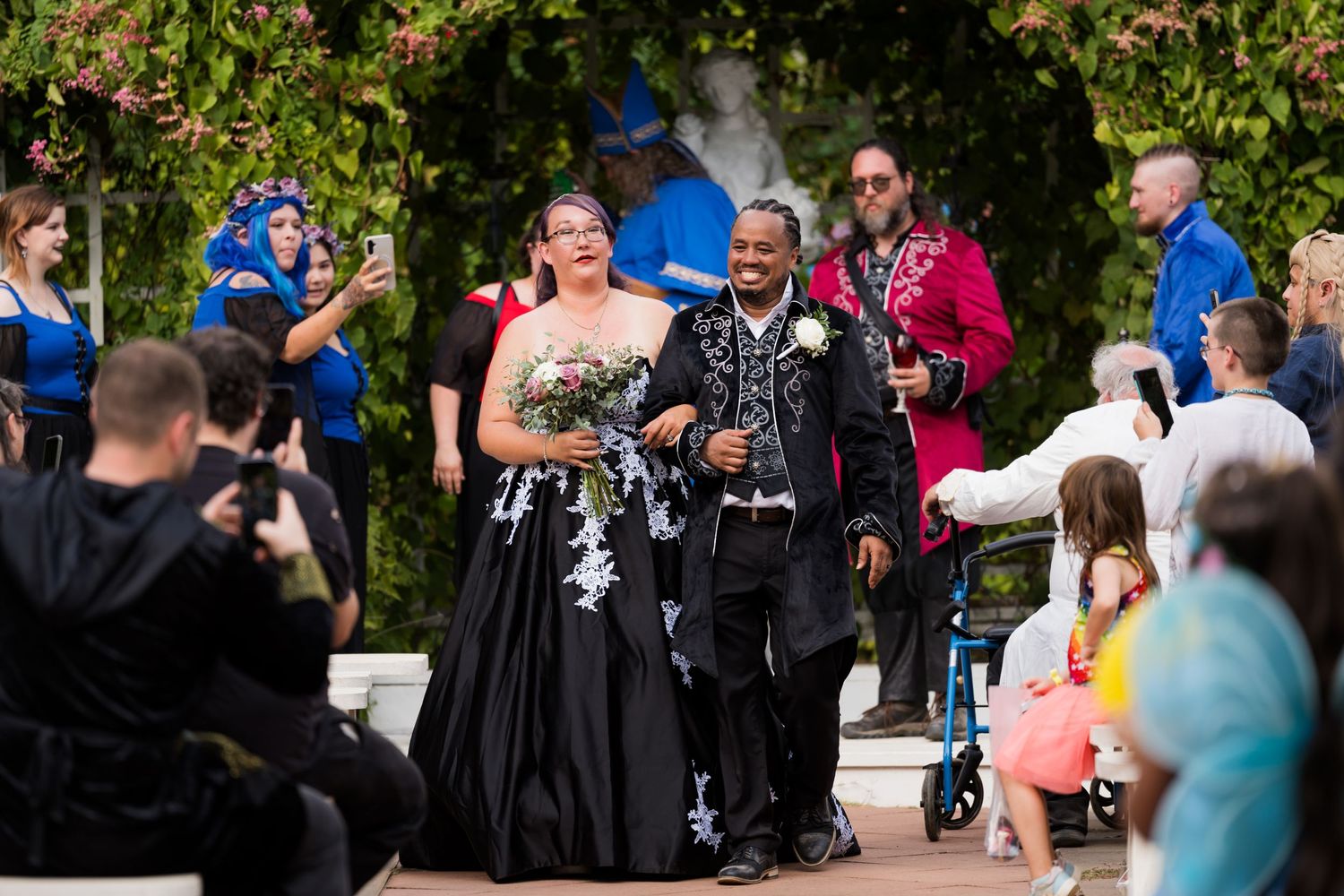 A wedding celebration takes place outdoors with attendees in formal and festive attire.