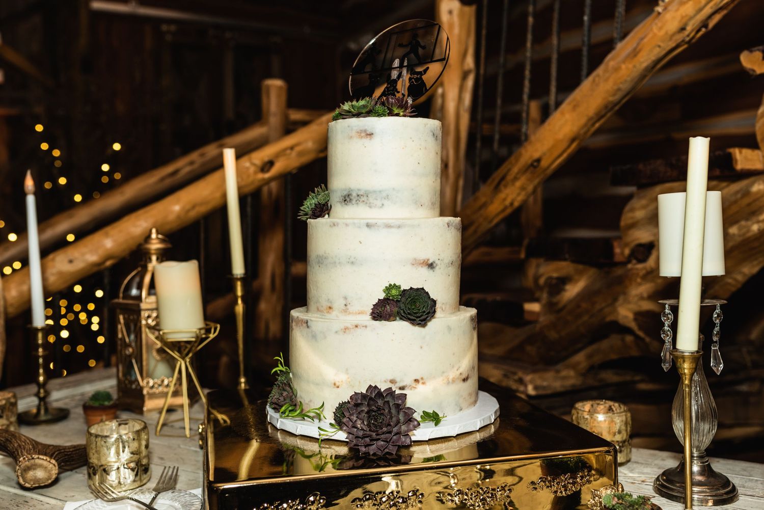 Elegant three-tier white wedding cake decorated with dark floral accents on a gold table setting.