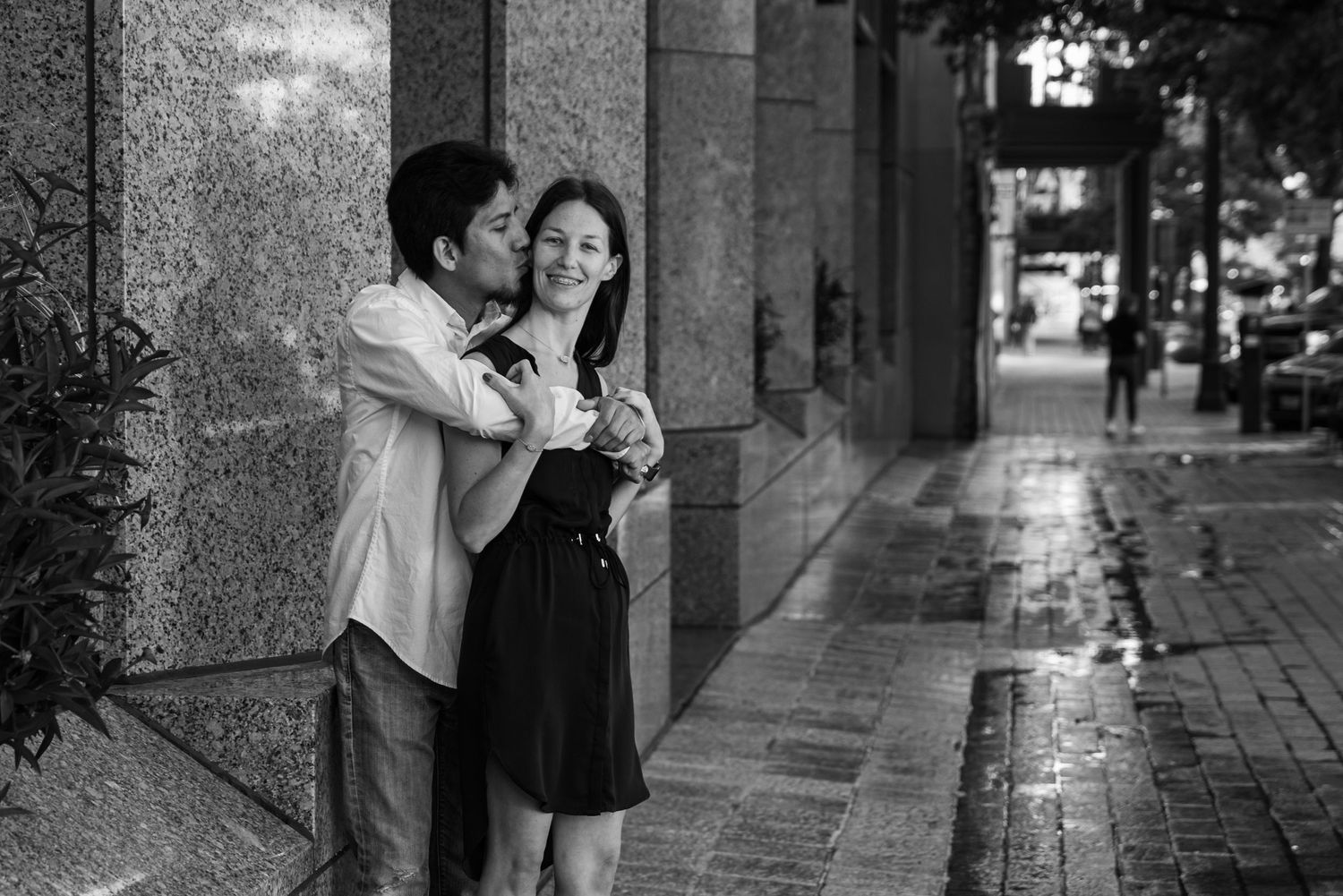 A black and white romantic moment captured on a rainy city sidewalk.