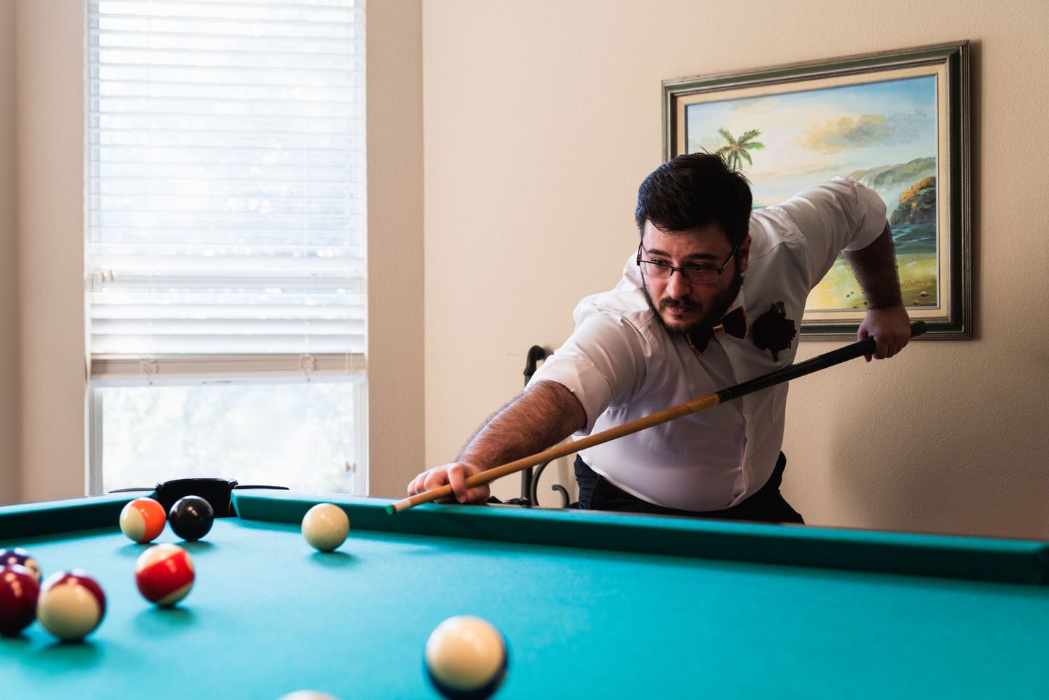 Person in casual attire takes aim while playing pool on a green felt table.