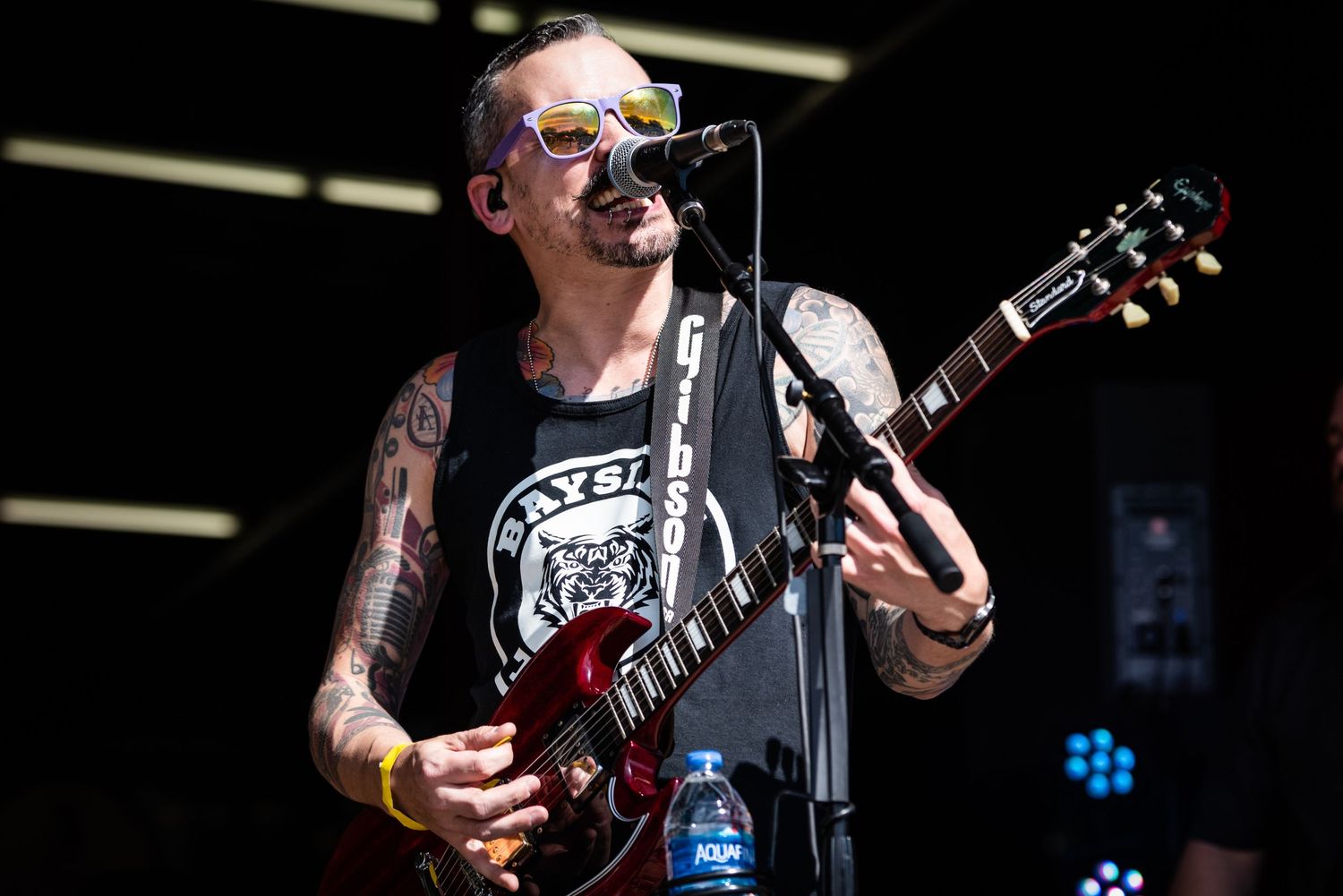 A close-up shot of a musician performing on stage with a red guitar and sunglasses.
