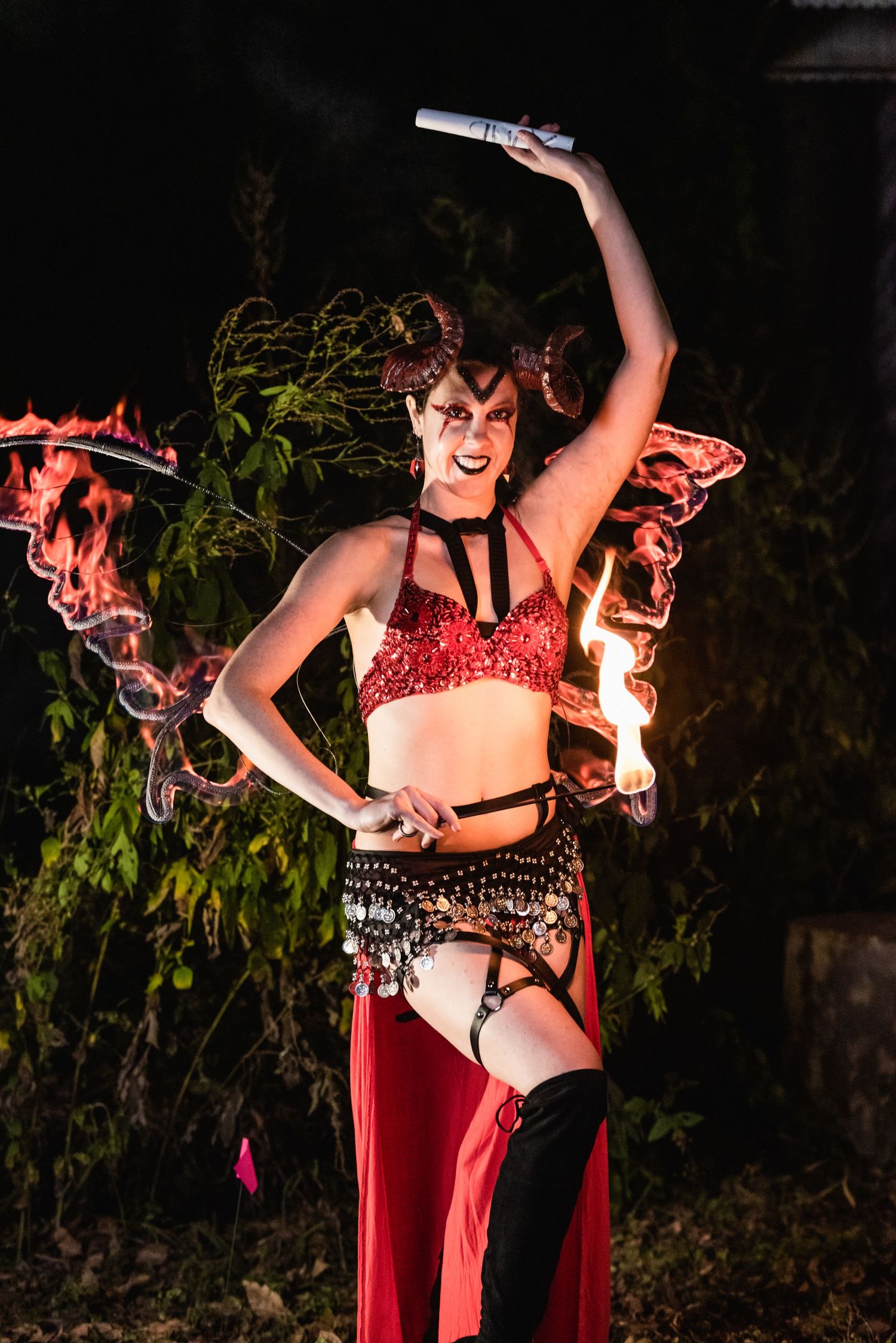 Performer in sparkly red costume strikes dramatic pose while fire dancing outdoors.