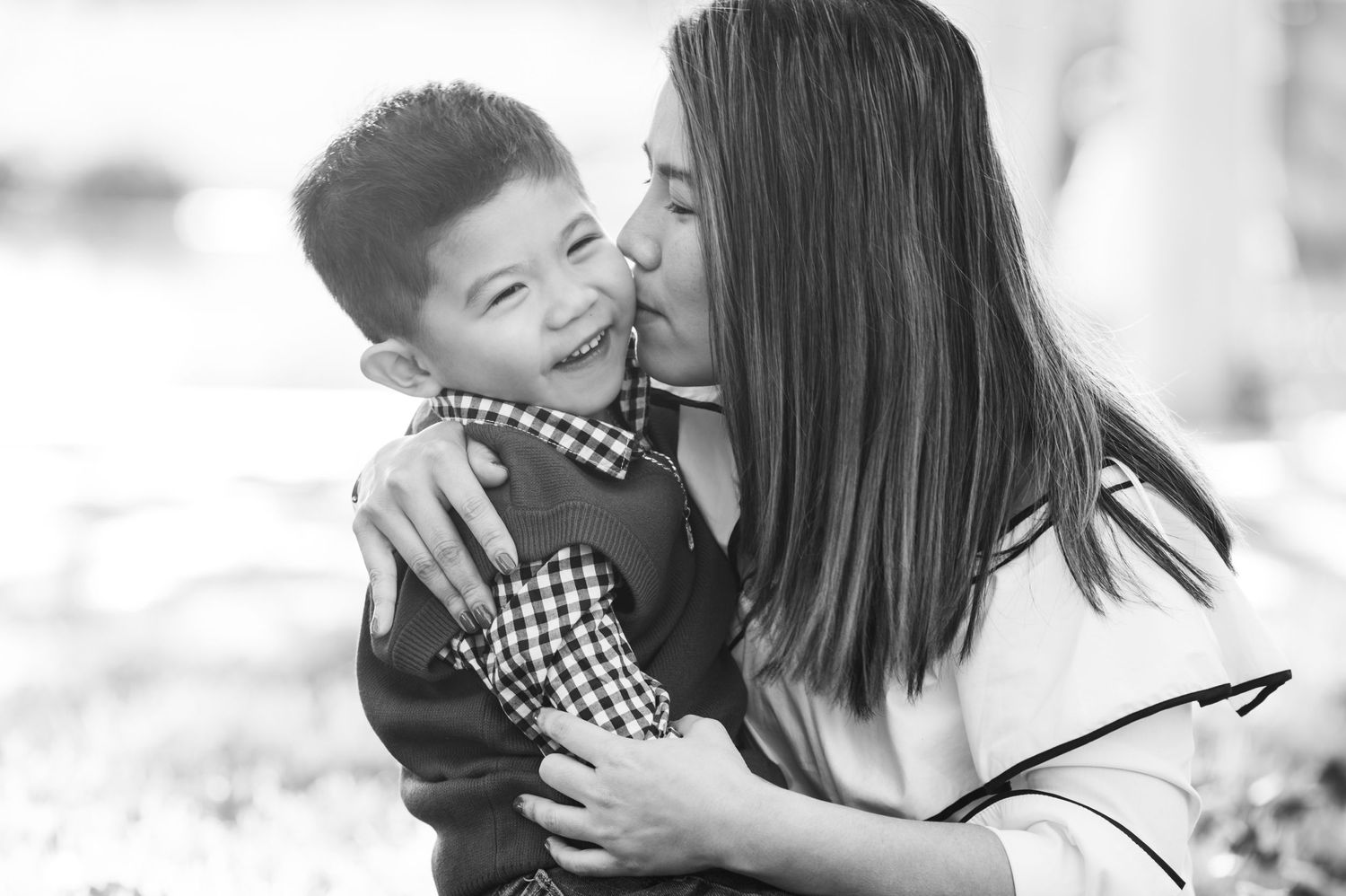 A tender moment captured in black and white as a parent shares a loving kiss with a young child.