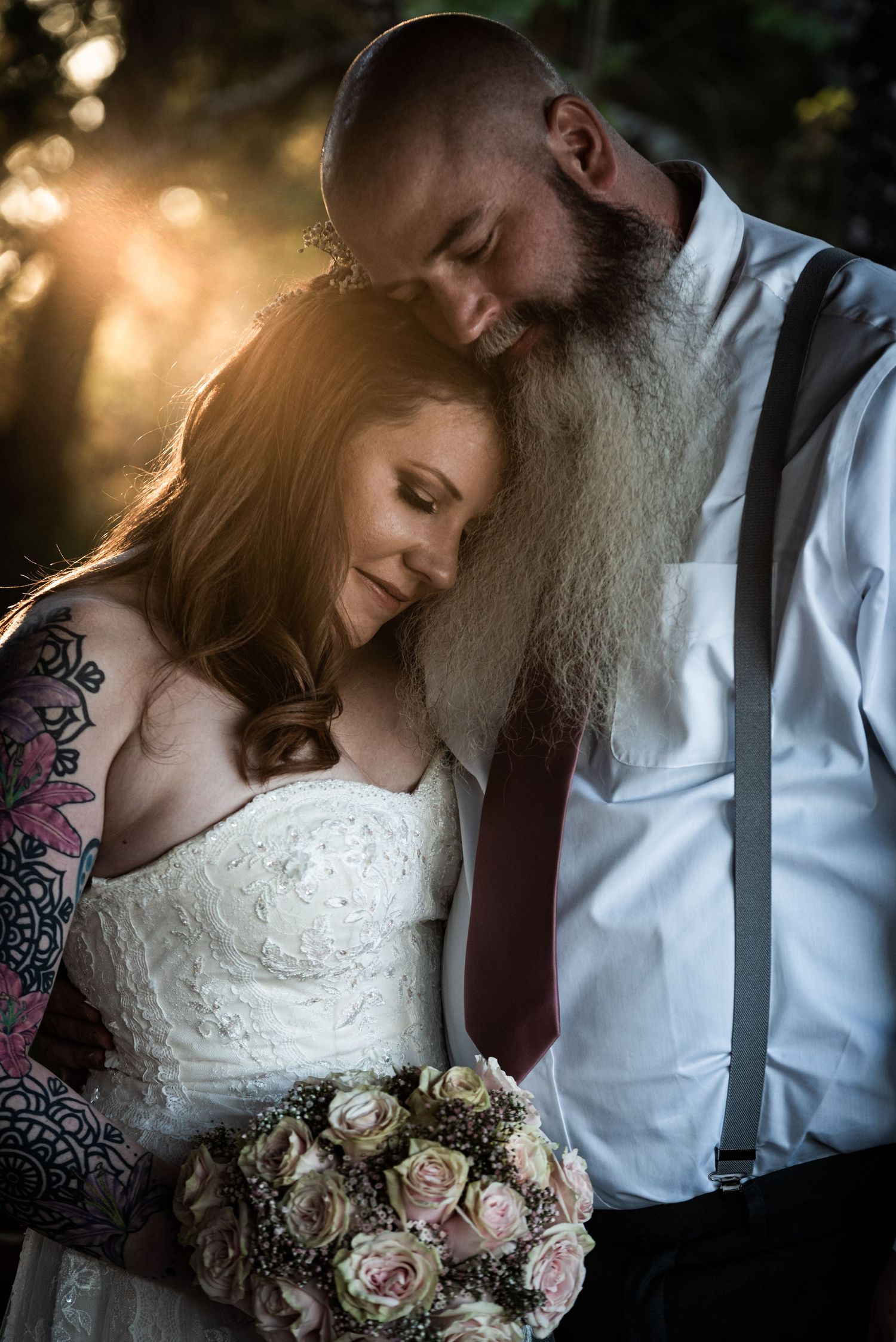 Golden sunset light illuminates a tender moment as couple poses with bouquet of pink roses.