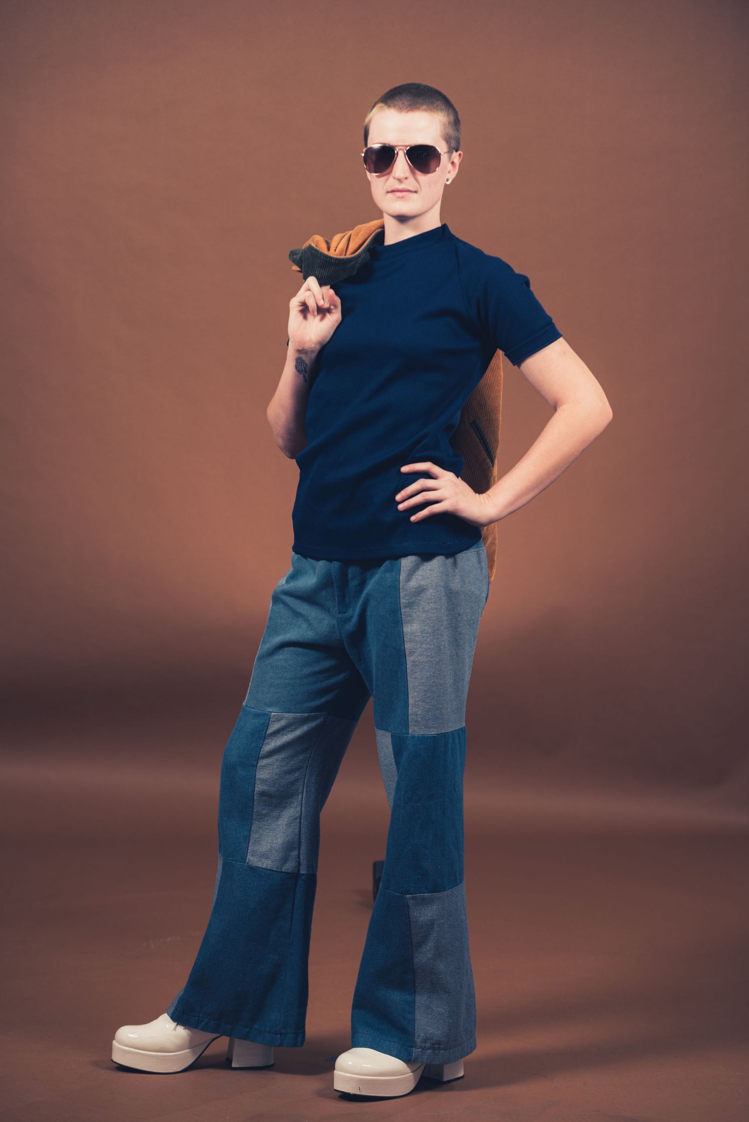 Stylish pose of person in navy shirt and patchwork jeans wearing sunglasses.