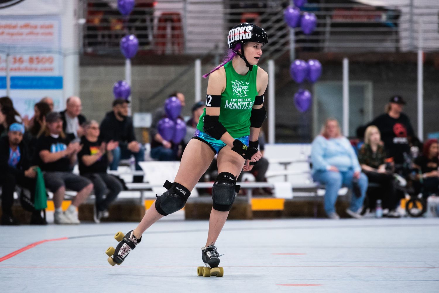 Roller derby athlete in green jersey skating with determination during competition.