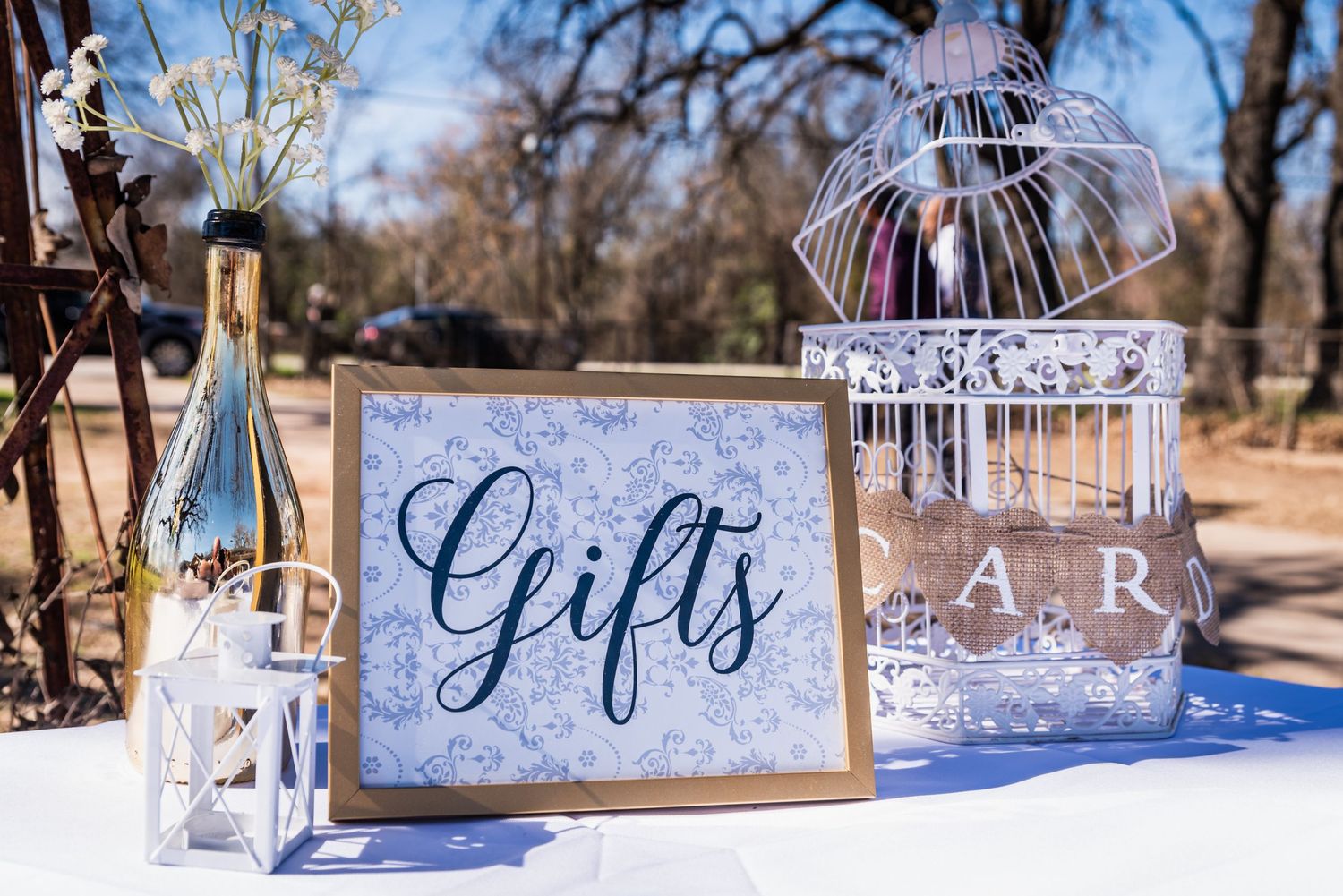 Wedding gift table setup with decorative birdcage and elegant signage on white tablecloth.