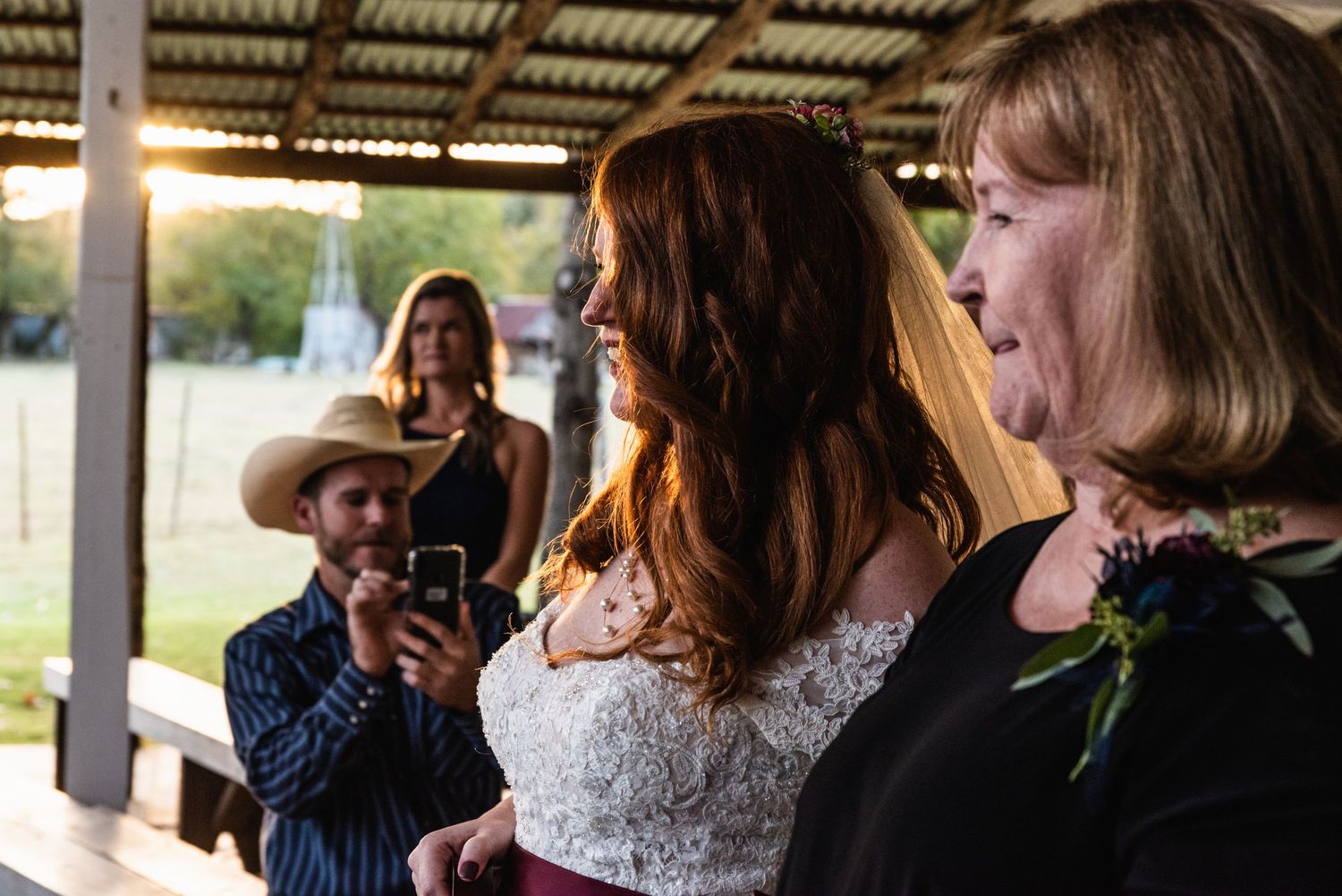 Wedding ceremony participants gathered under a covered outdoor venue with natural lighting.