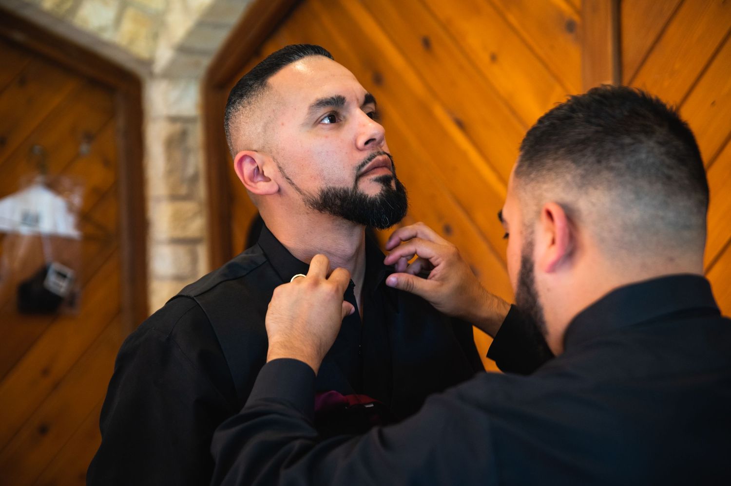 A person adjusts their beard while looking in a mirror in a rustic wooden interior setting.