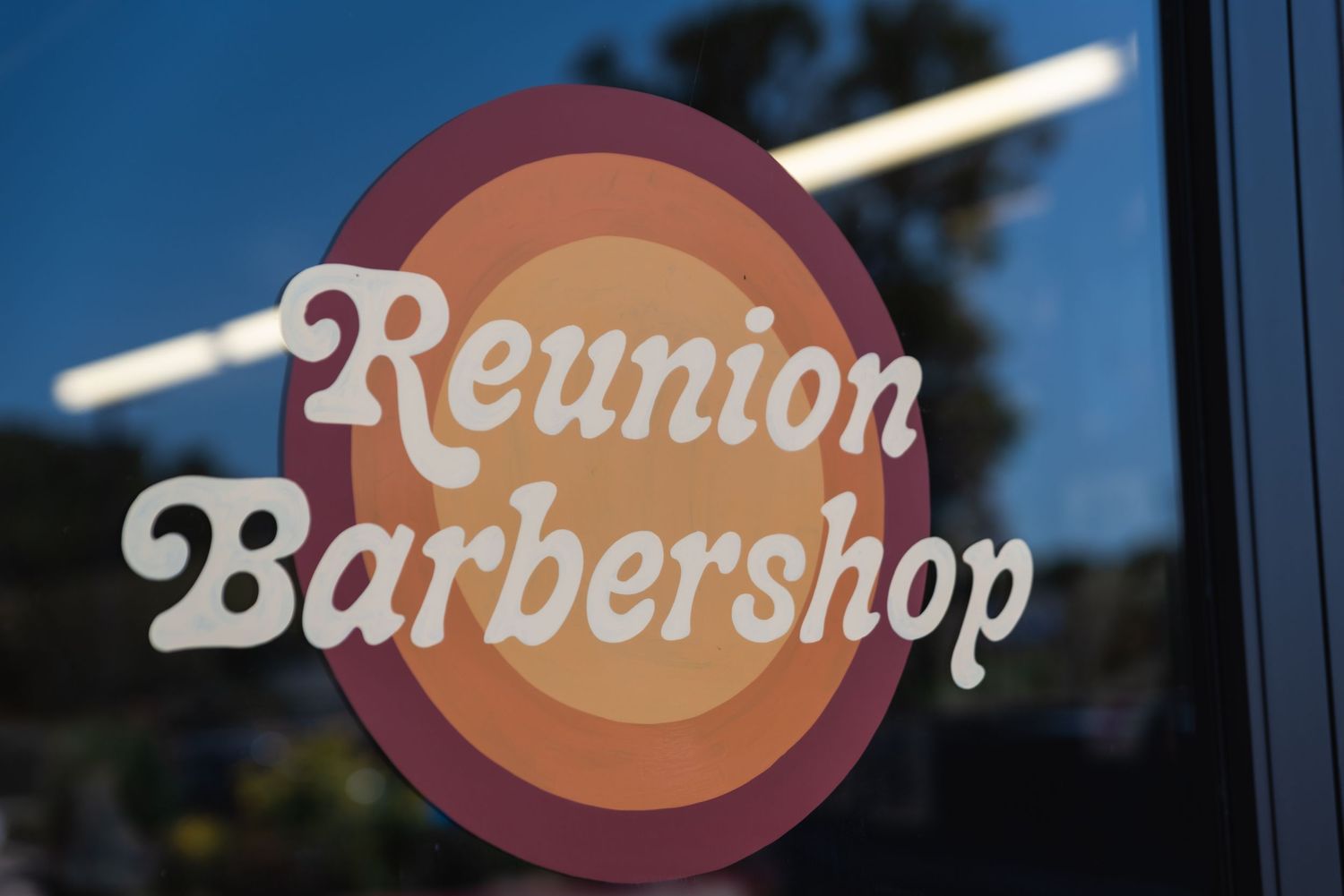 Exterior shot of Reunion Barbershop storefront sign with retro-style lettering.