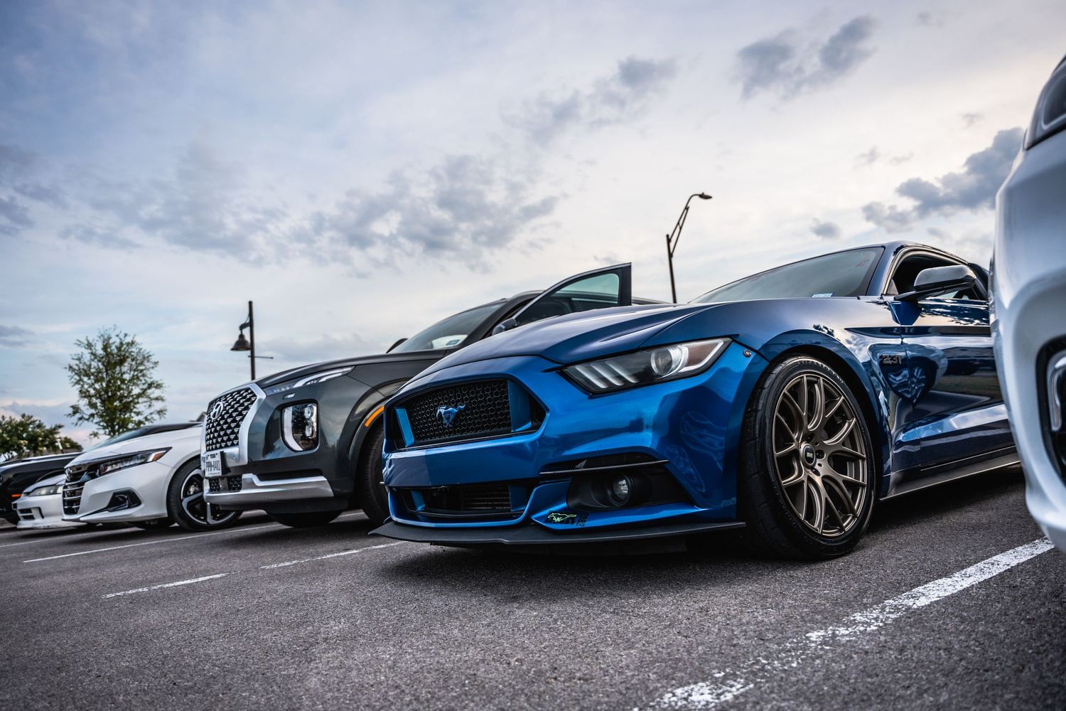 Low angle shot of a bright blue Ford Mustang with custom wheels parked in a lot.