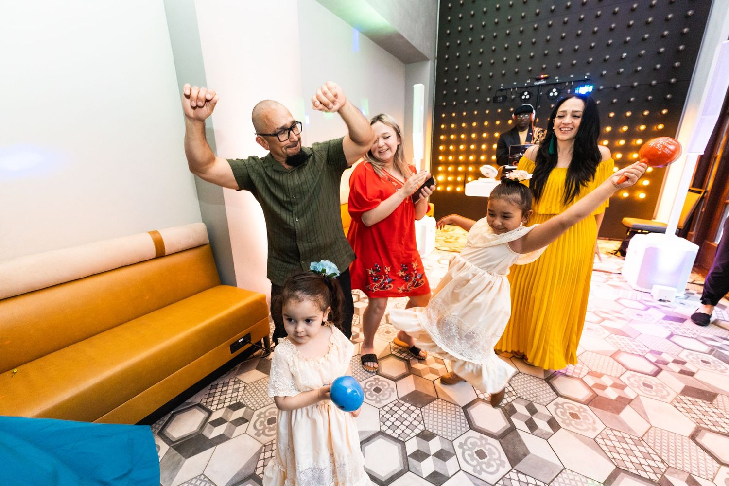 Group of people dancing enthusiastically in a venue with patterned floors and bench seating.