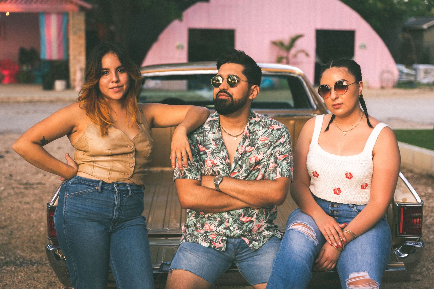 Three friends in casual summer attire pose together against a pink wall background.