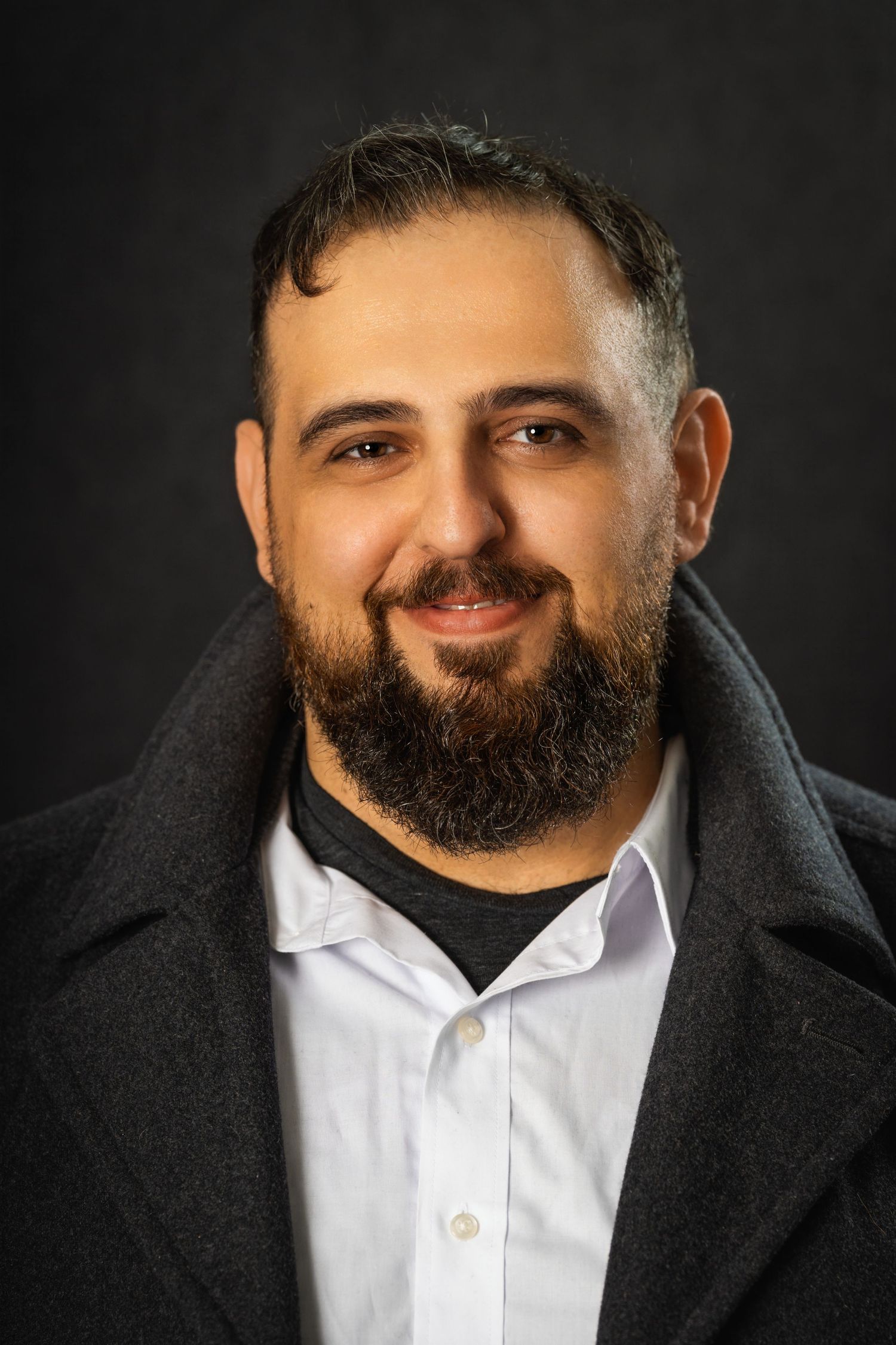 Professional headshot of a bearded man in business attire against a dark background.