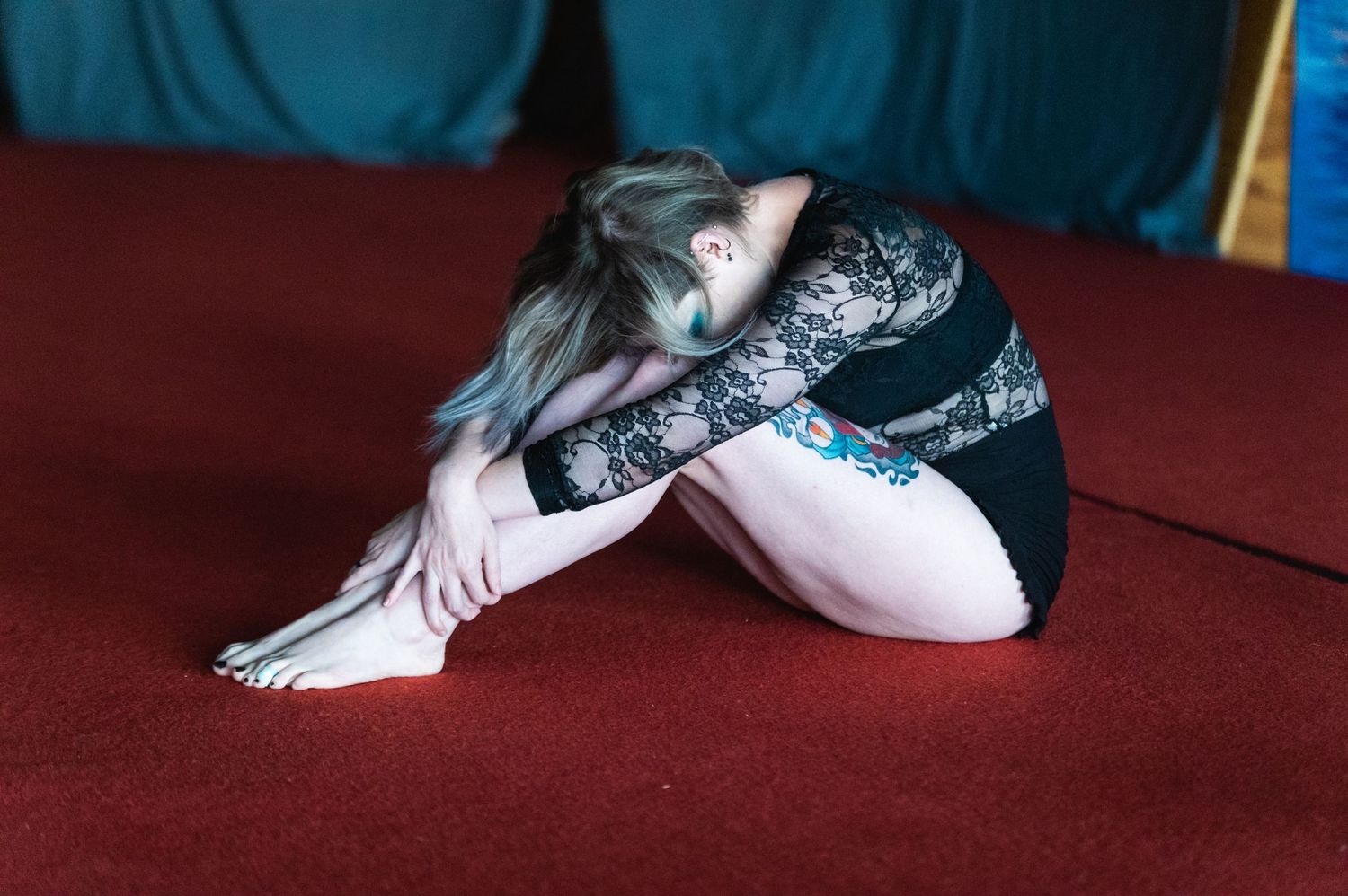Dancer in lace costume stretches on red surface during performance preparation.