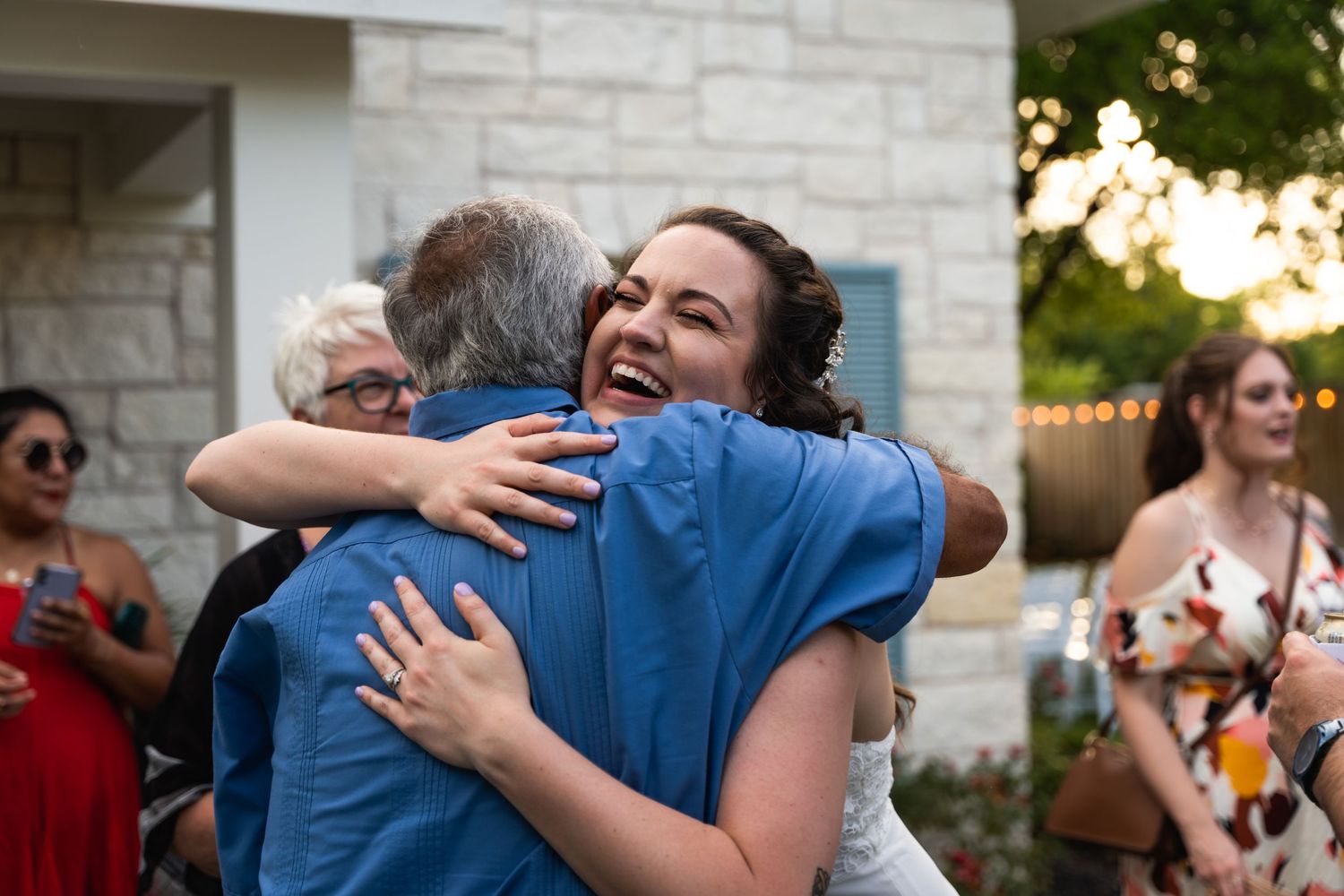 Joyful embrace captured during outdoor celebration with guests in background.