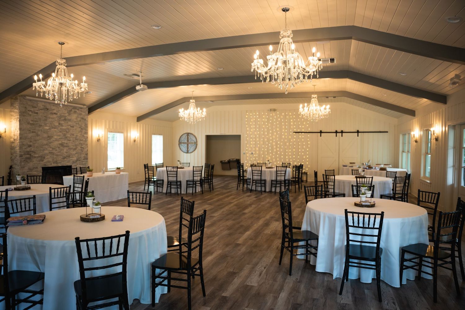 Elegant wedding venue with crystal chandeliers, white tables, and dark wood flooring.