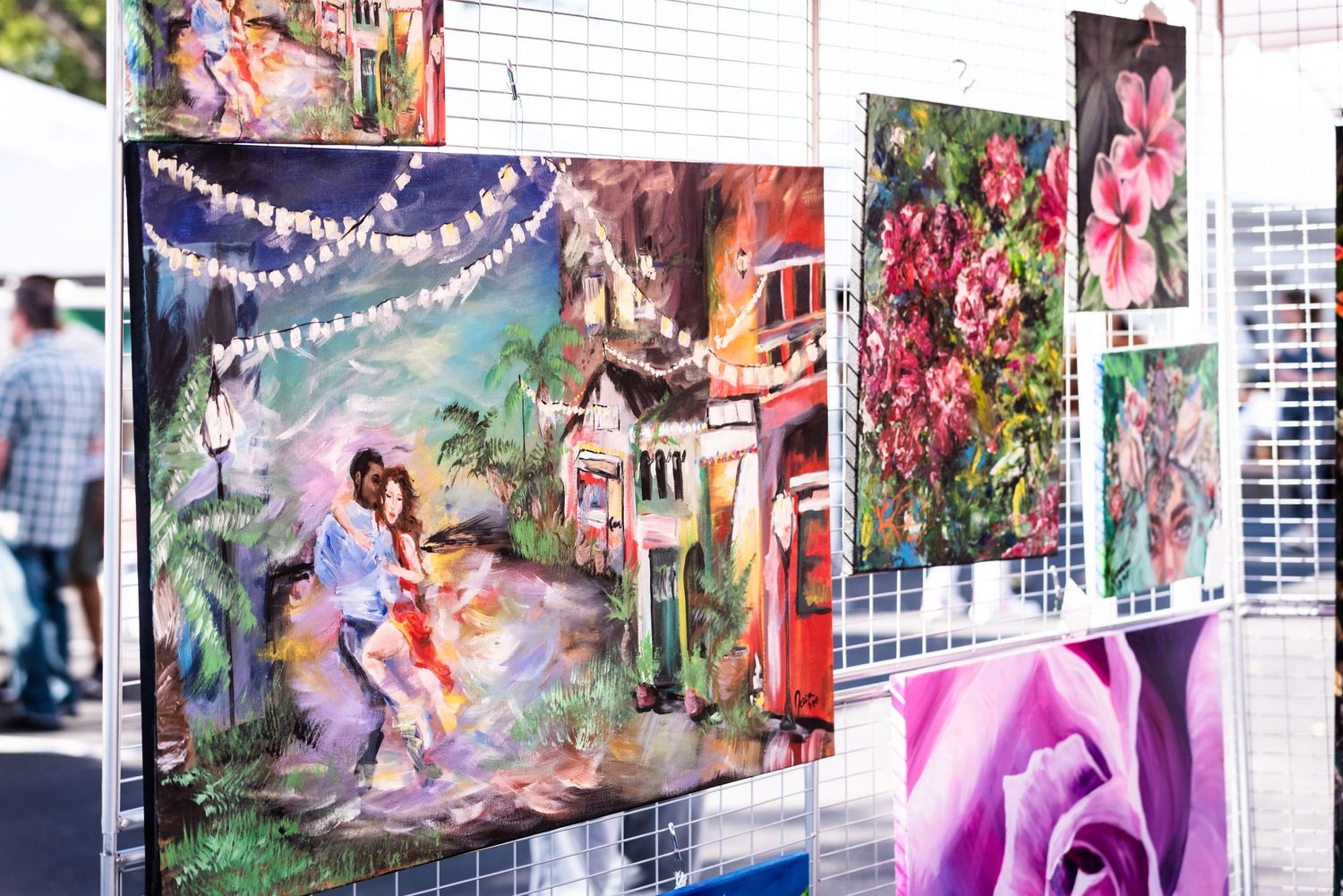Colorful artwork displays featuring romantic illustrations and floral scenes hung on gallery wall.