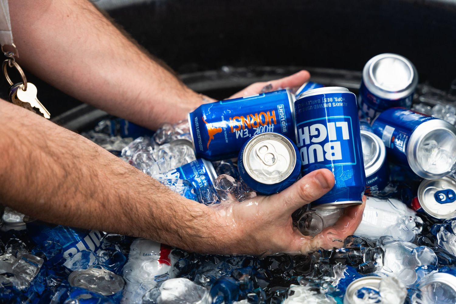 Close-up of hands grabbing Bud Light cans from ice-filled cooler.