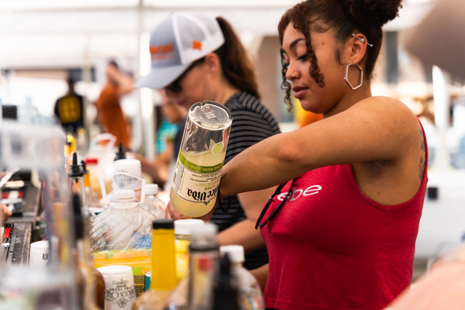 Bartender in red tank top preparing cocktails at outdoor bar station.