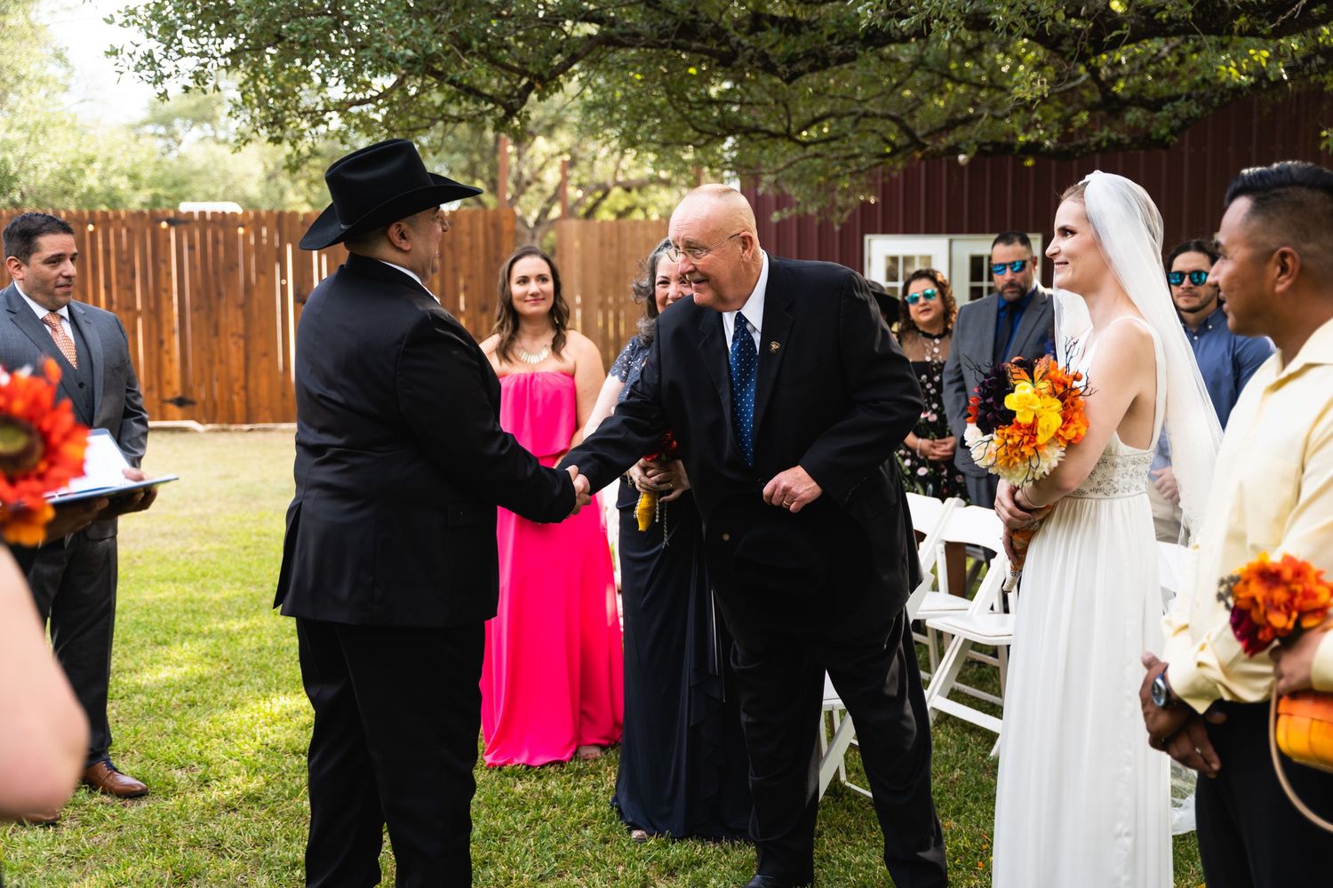 A celebratory handshake during an outdoor wedding ceremony with guests looking on.