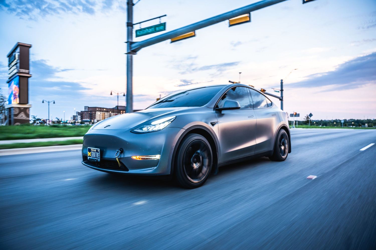 Tesla Model Y in matte finish with black wheels cruising on highway during sunset.
