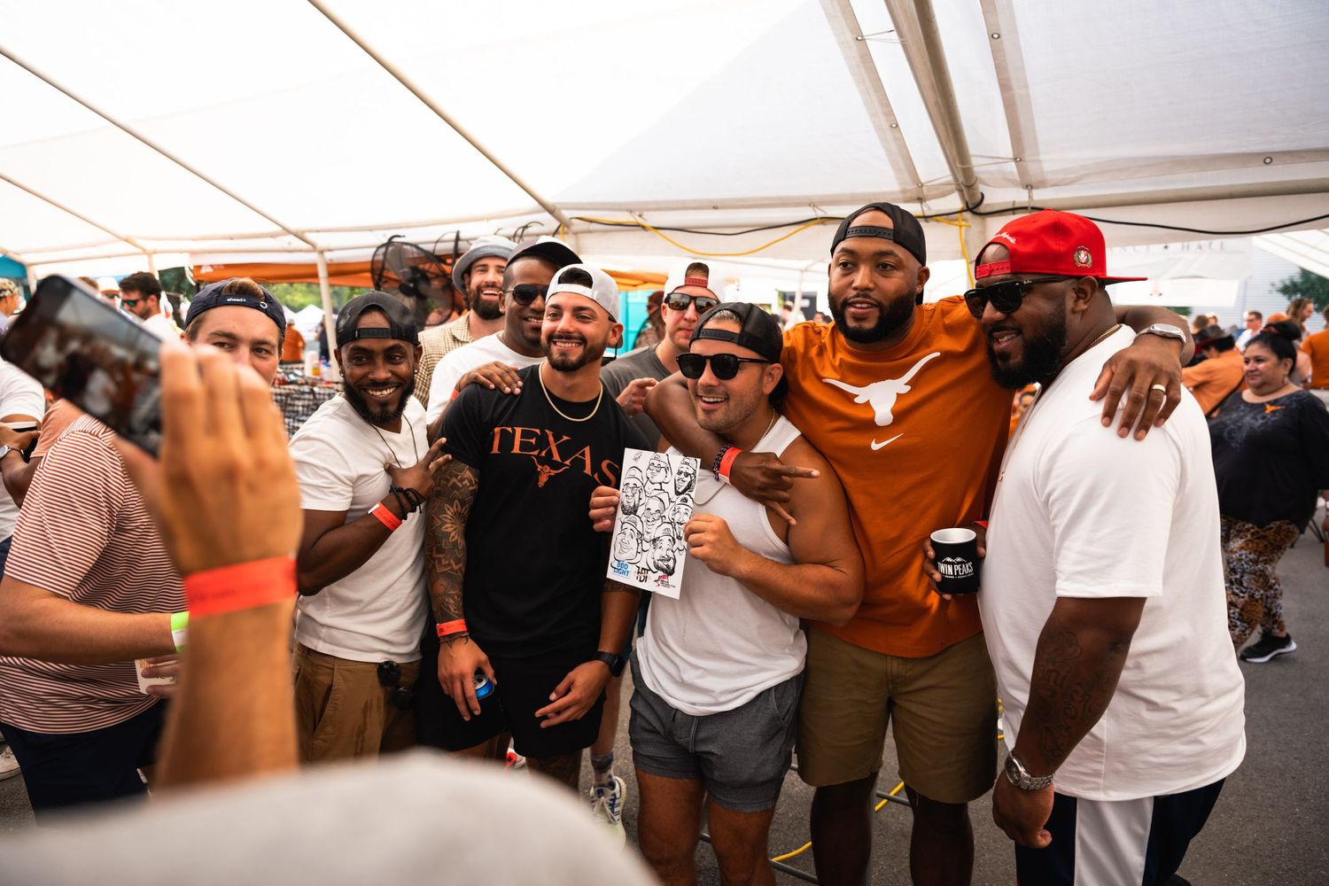 Crowd of partygoers cheering and celebrating together under a white event tent.