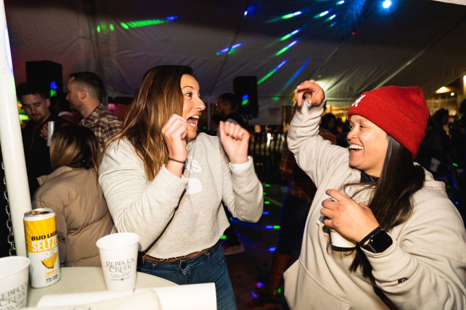Friends dancing and singing together at a party with disco lights in the background.
