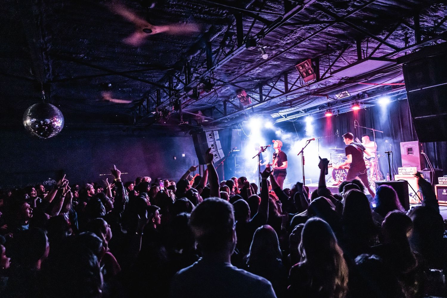 A concert crowd watches performers on stage under dramatic purple and blue lighting.