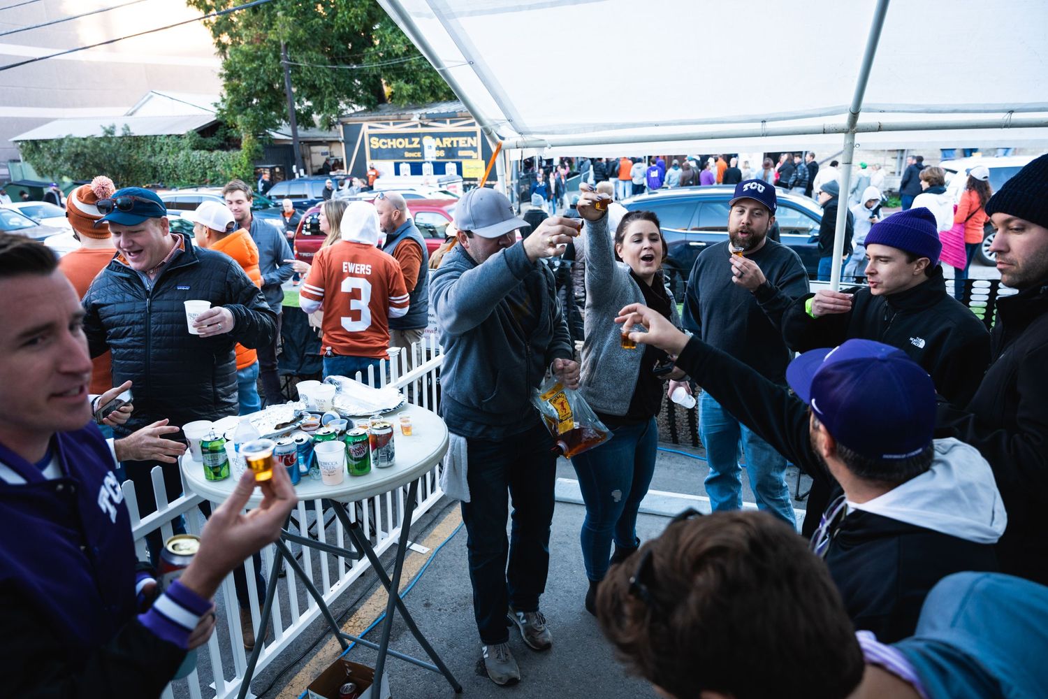 Crowded outdoor tailgate party with fans in sports jerseys mingling under a tent.