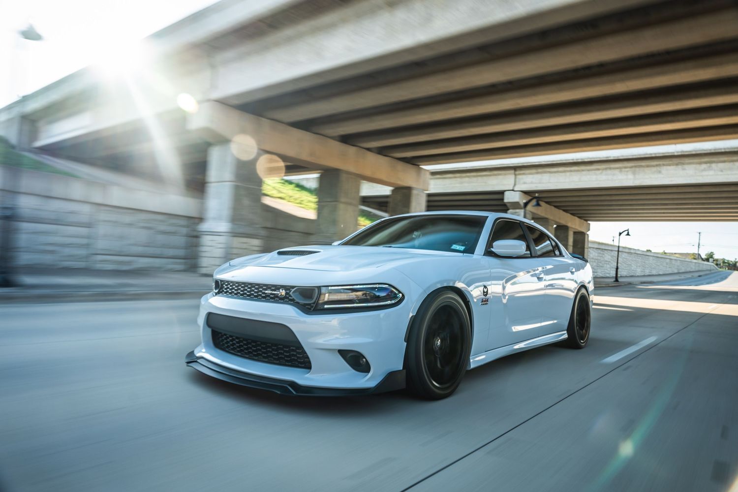 White Dodge Charger with black wheels photographed in motion under highway overpass.