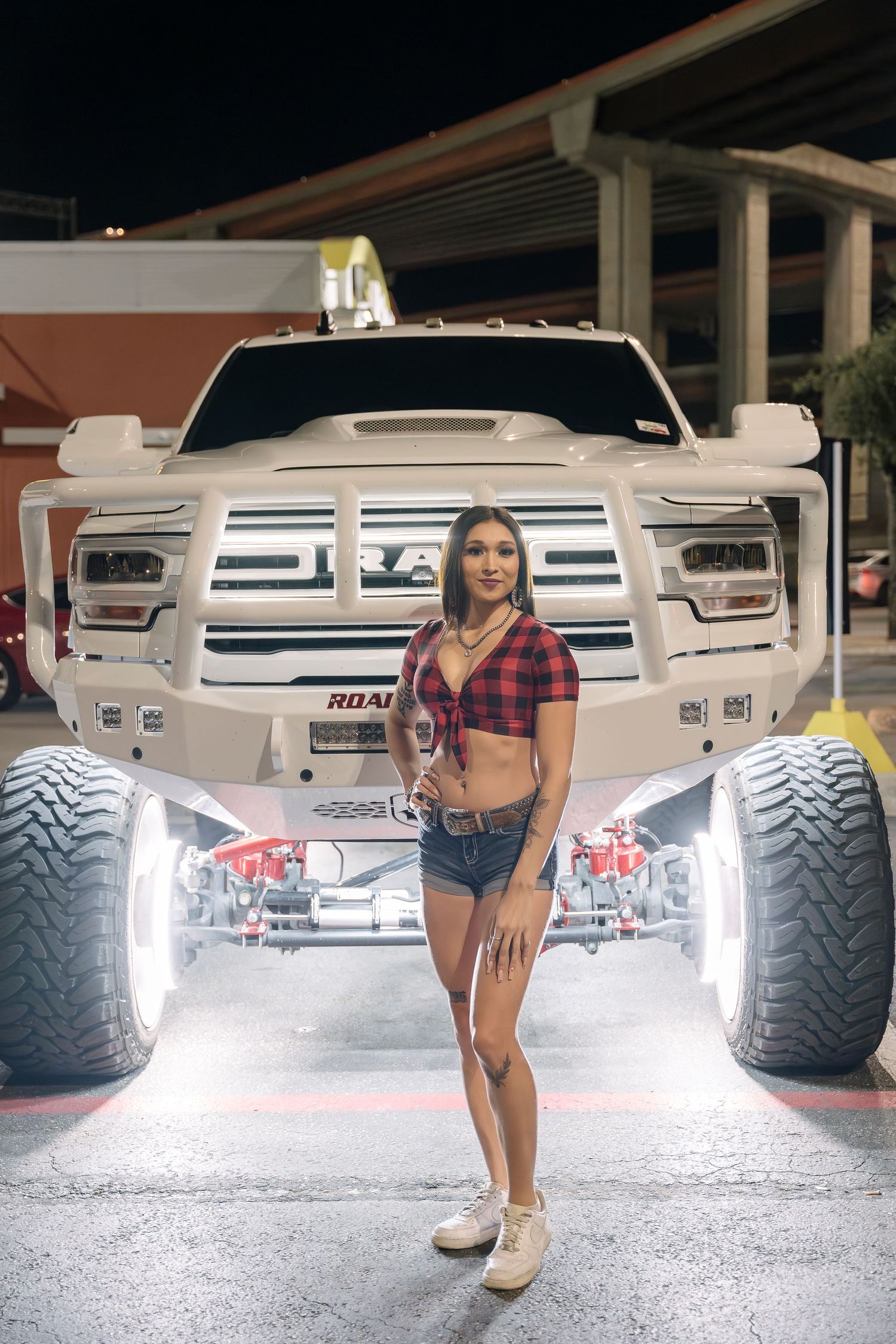 Custom lifted white RAM truck with illuminated undercarriage and large off-road tires.