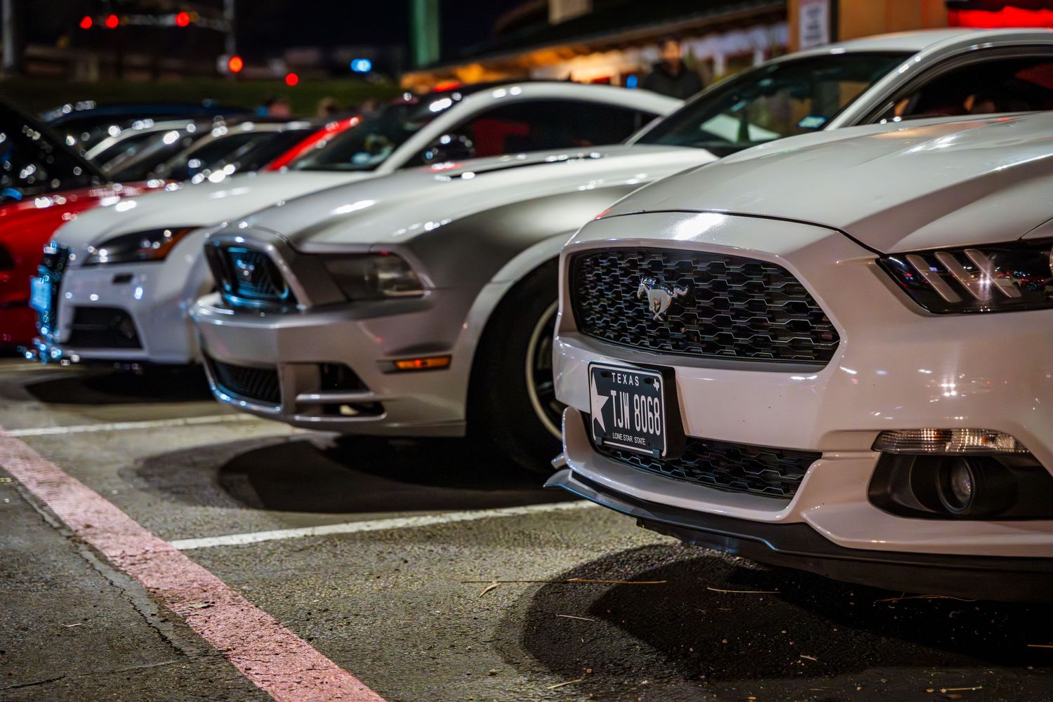 Row of modern sports cars including Mustangs parked in a parking lot at night.