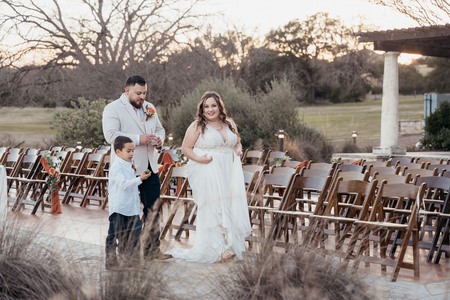 A couple walks through an outdoor wedding venue with rustic wooden chairs.