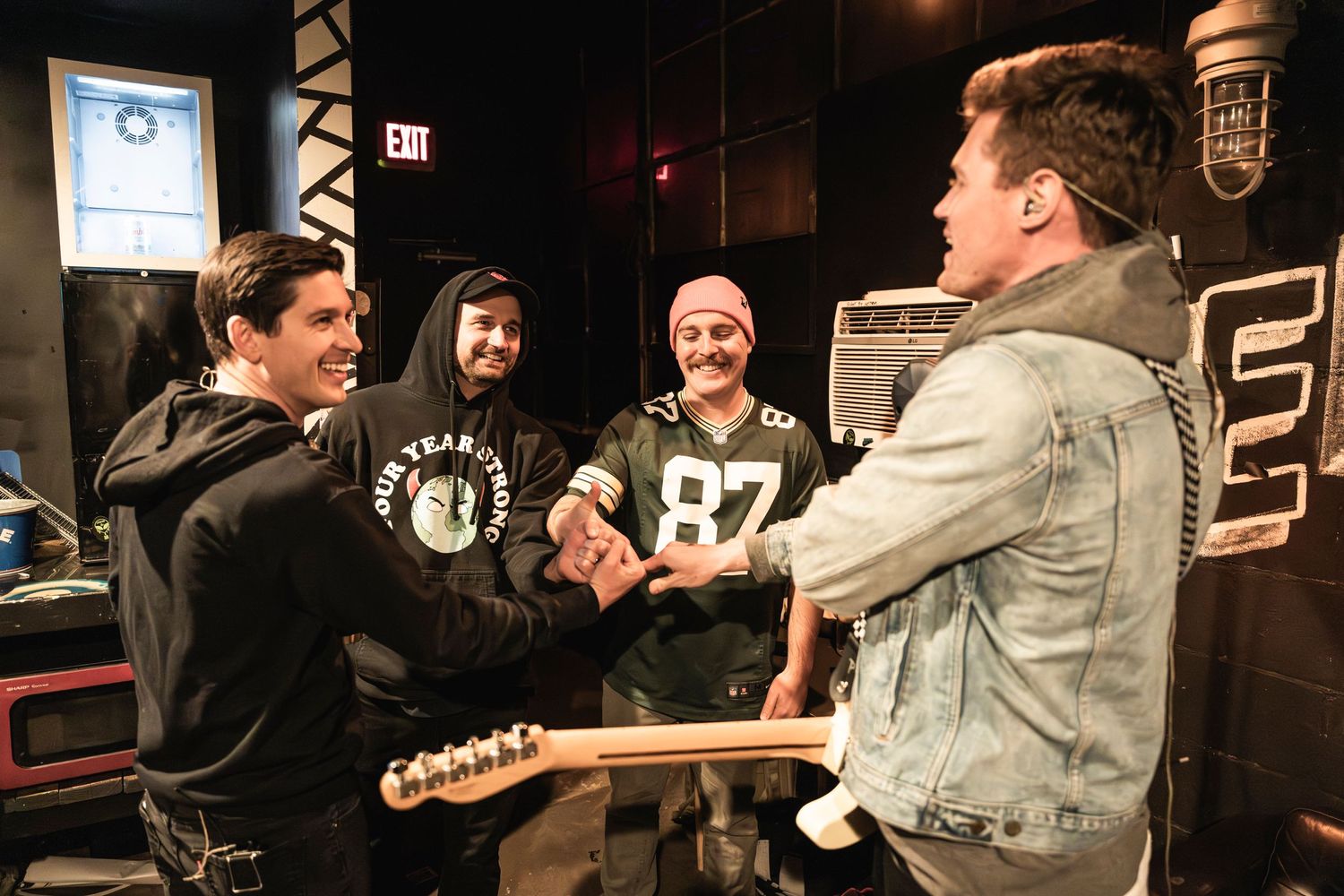 Musicians interacting enthusiastically in a backstage area with Empire signage.