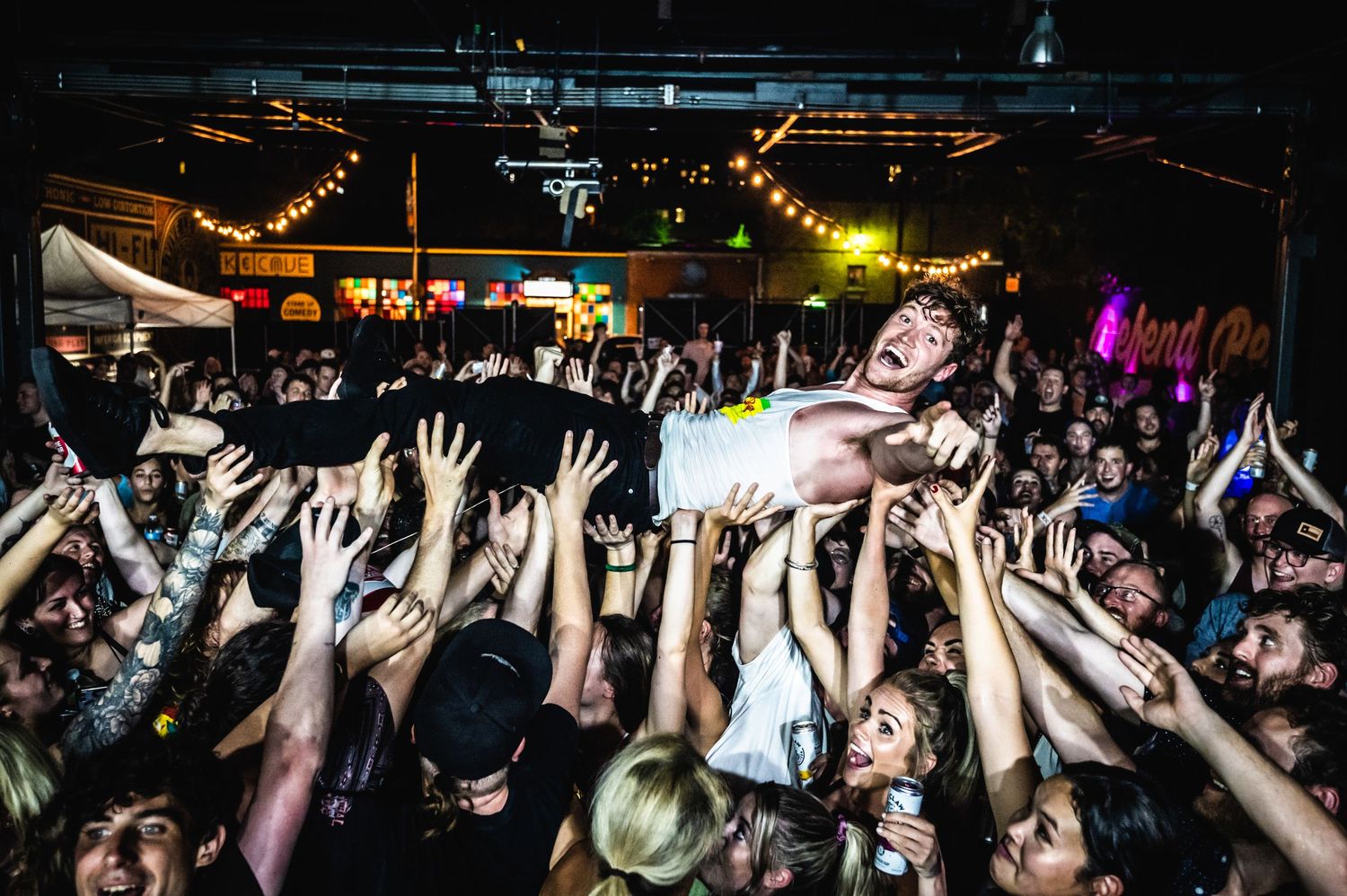 Concert crowd raises hands in the air during an energetic performance in a dark venue.